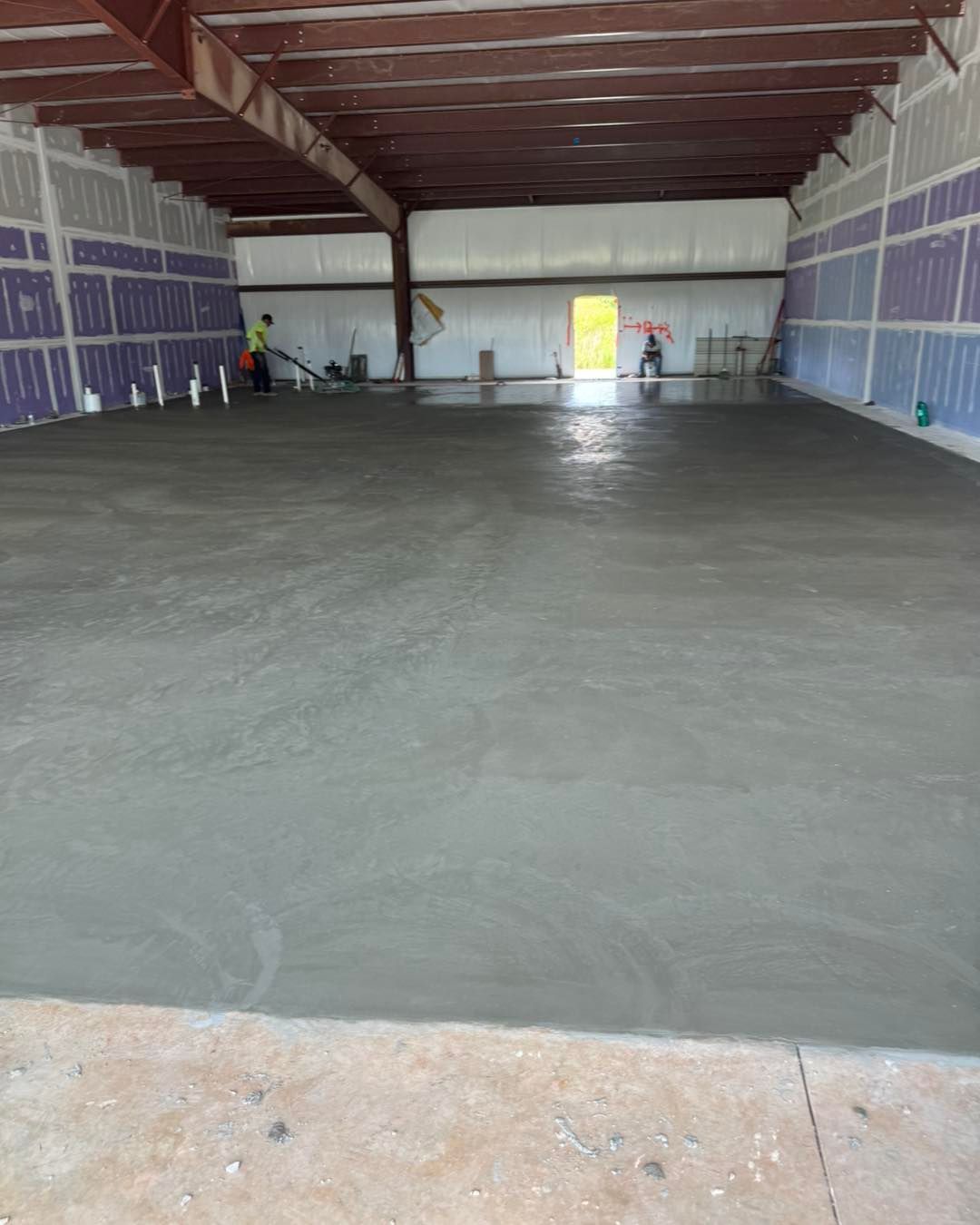 Large unfinished indoor warehouse with a freshly poured concrete floor and exposed ceiling beams.