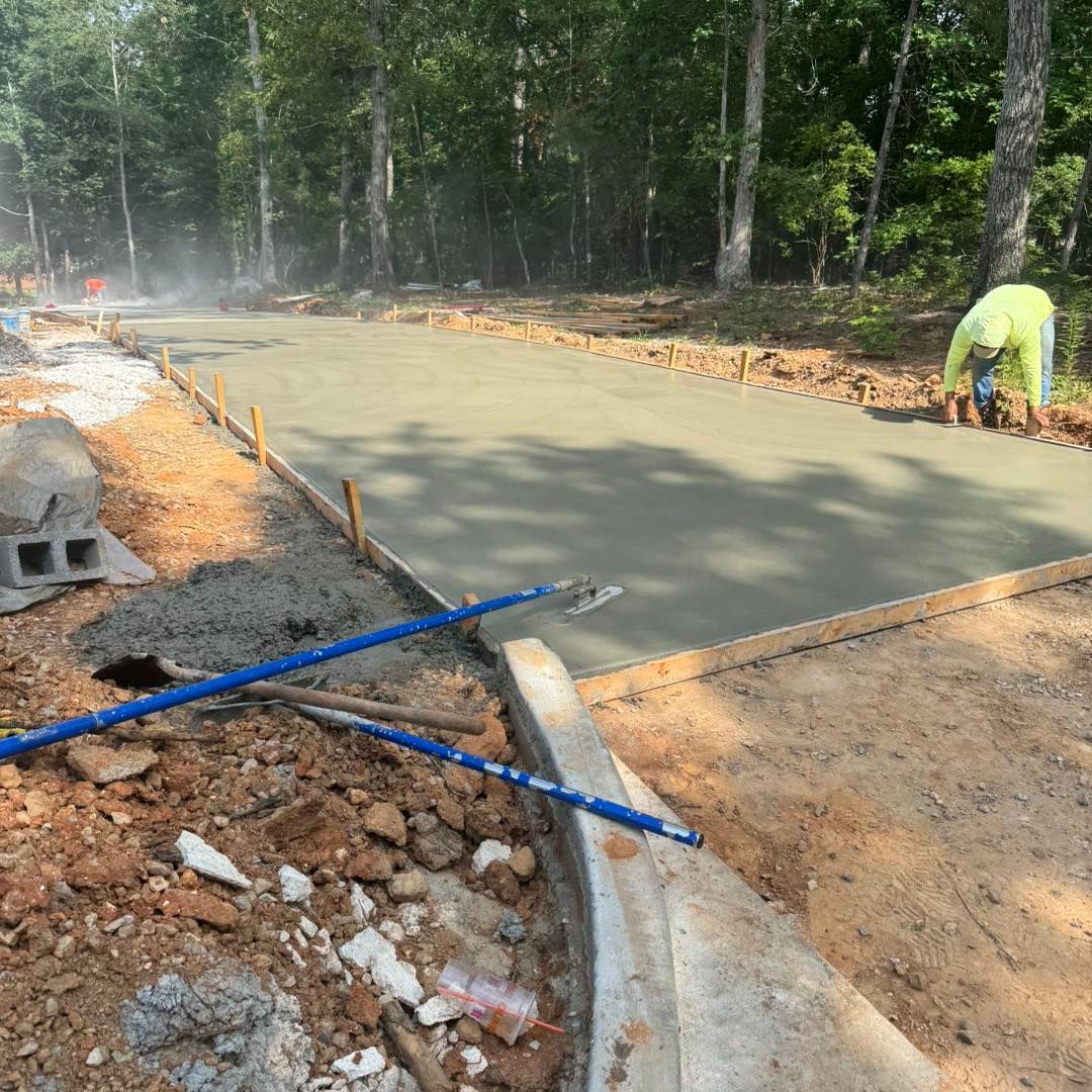 Fresh concrete slab being poured at a roadside construction site, with workers and forest background.