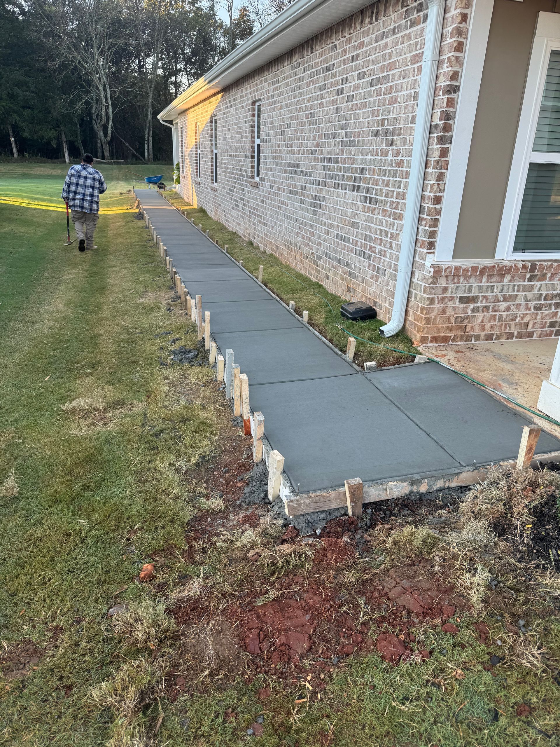 Sidewalk repair along a brick building, with a person walking away on the grass nearby.