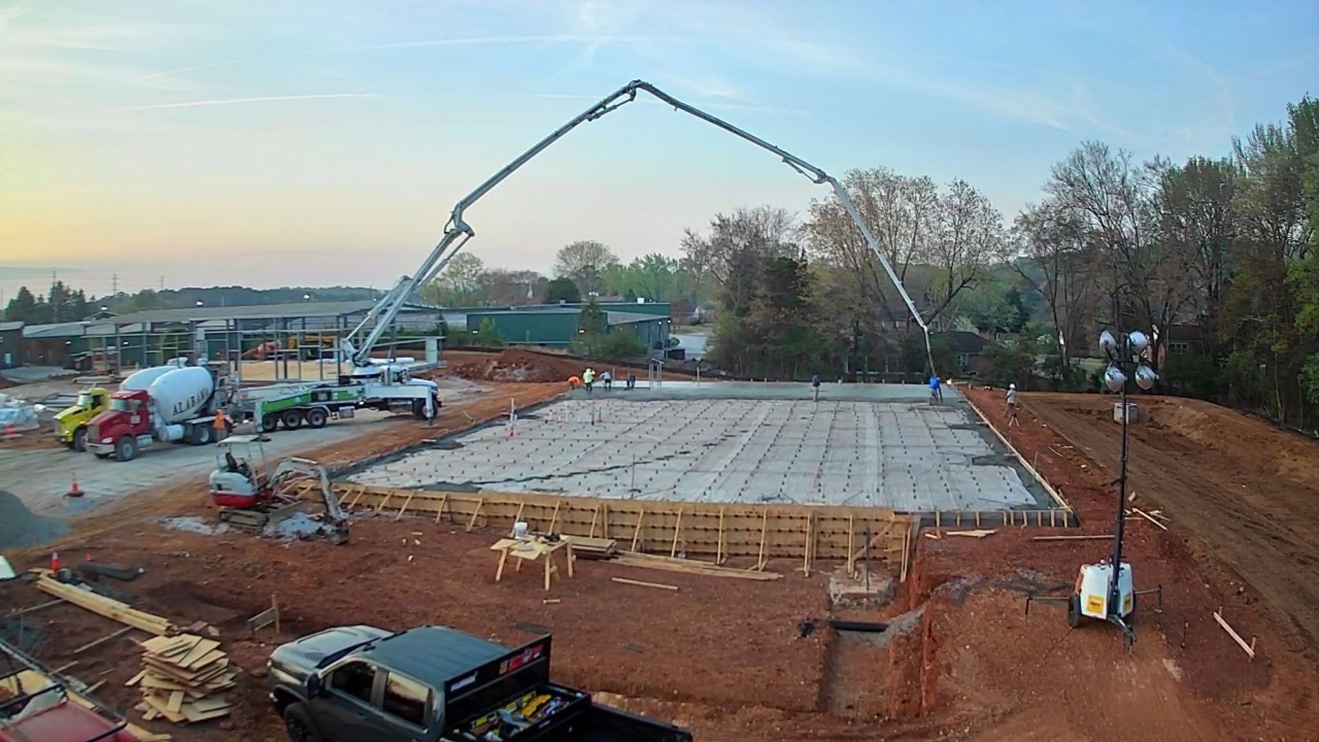 Concrete foundation under construction with a concrete pump truck arching over the site at dusk