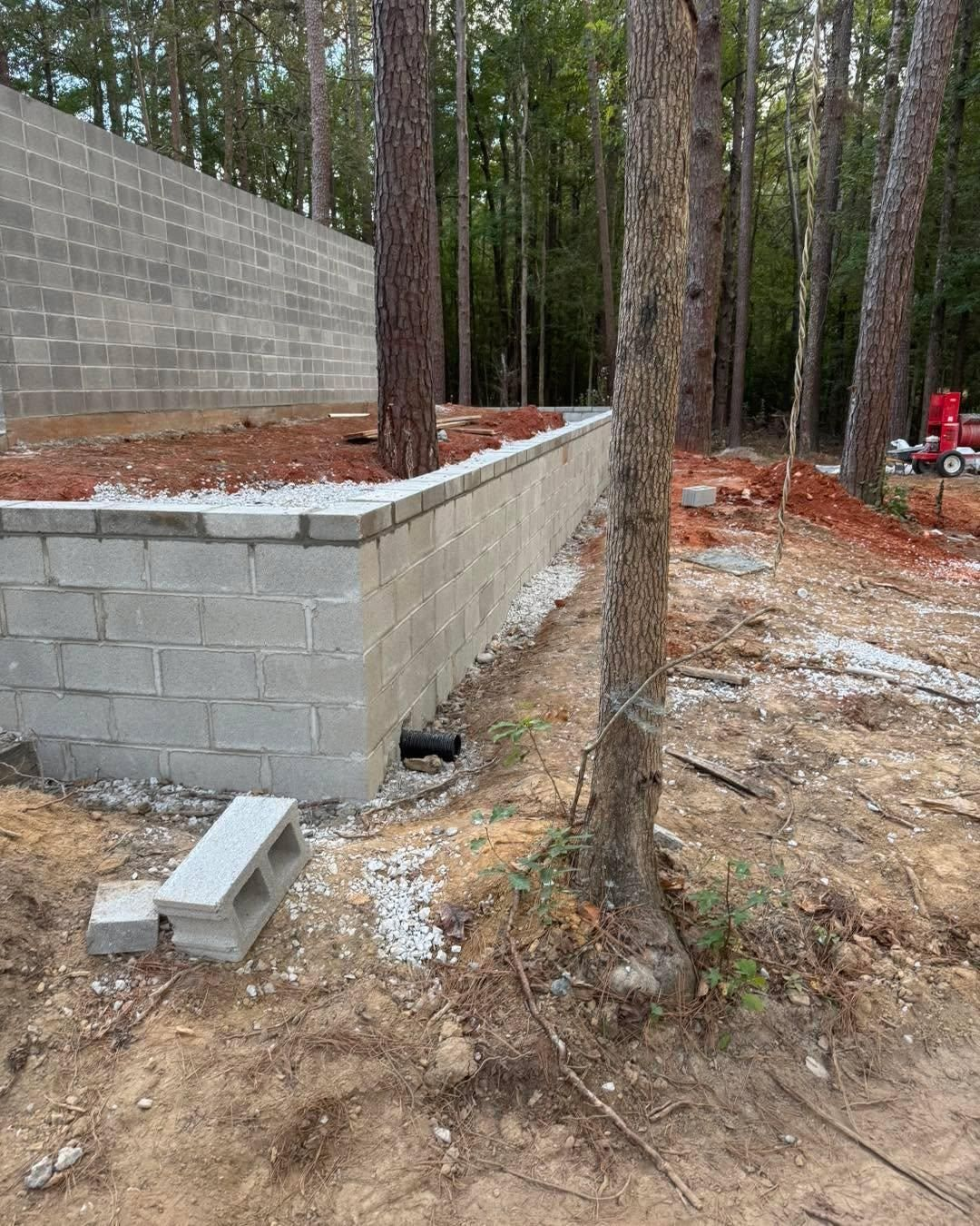 Concrete retaining wall and steps under construction in a wooded area, with a red toy vehicle in the background.