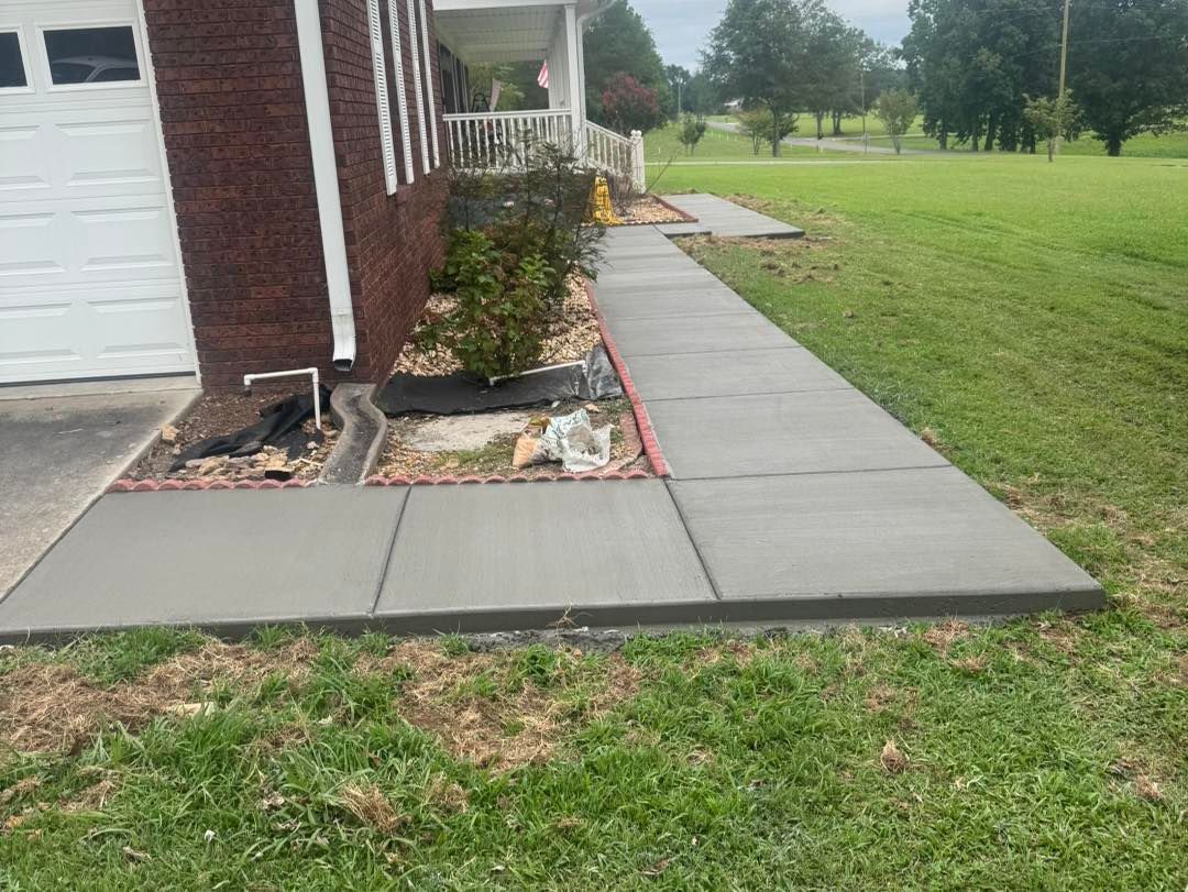Concrete walkway along a brick house beside a green lawn and landscaped bed