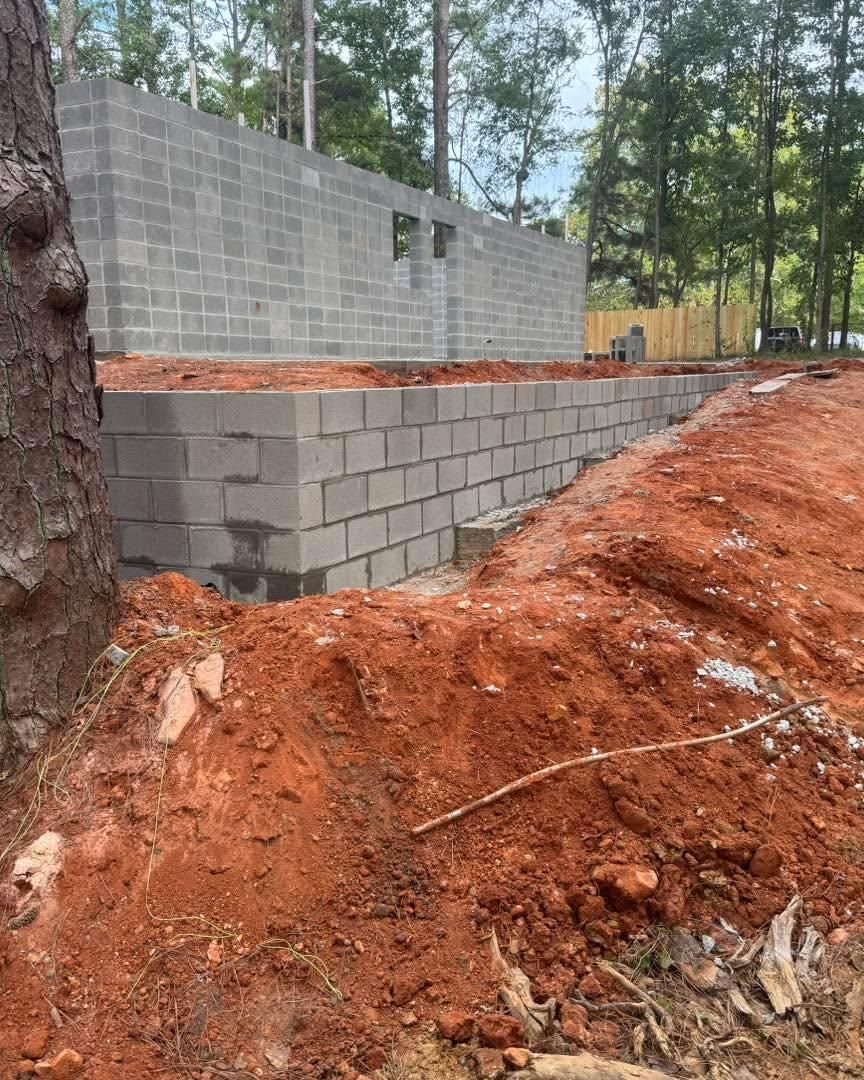 Concrete block foundation under construction beside red dirt and pine trees