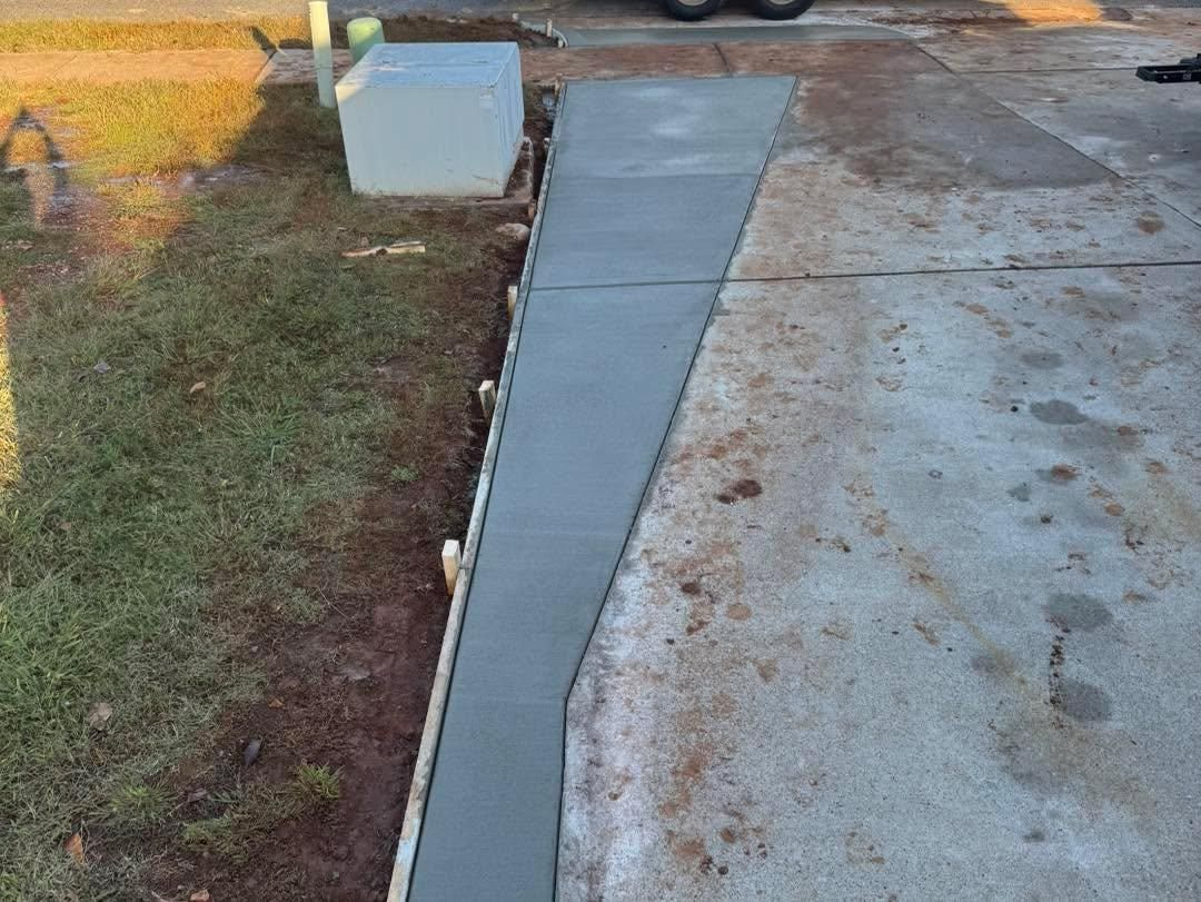 Concrete walkway beside grass and a driveway, with a new gray sidewalk section.