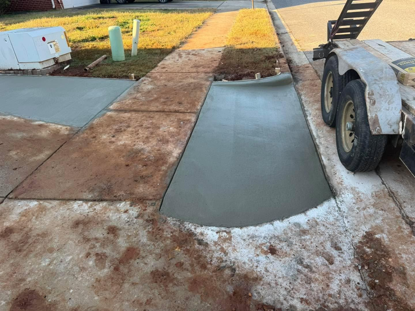 Fresh concrete sidewalks and curb cuts under construction beside a street, with a trailer at right.