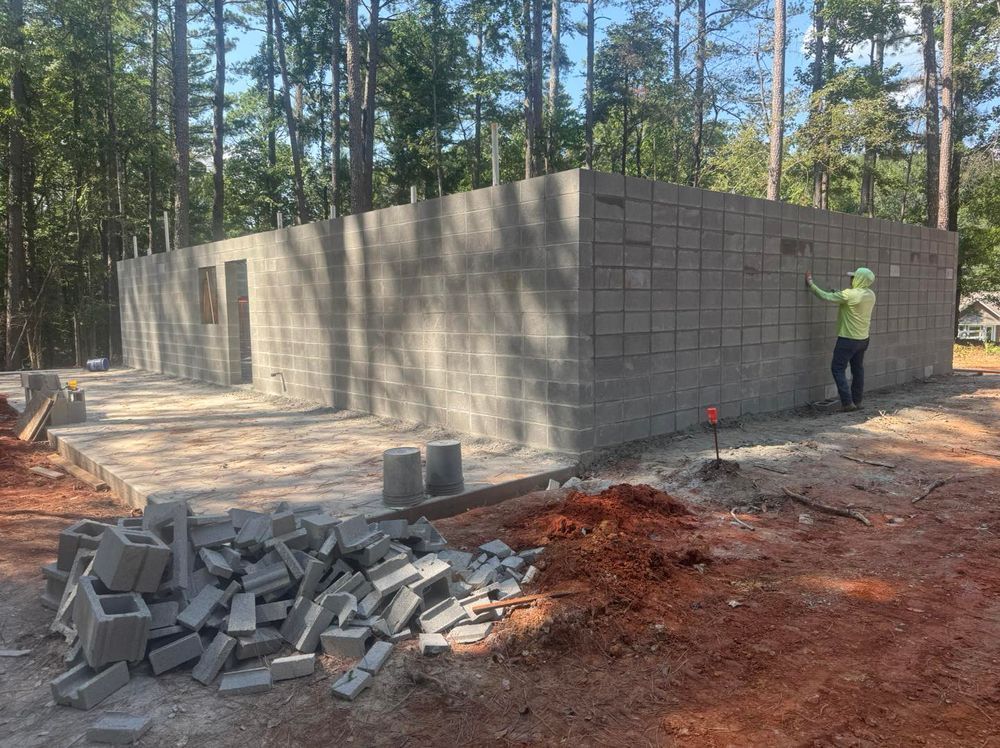 Construction worker standing beside a cinder block wall at a building site in a wooded area