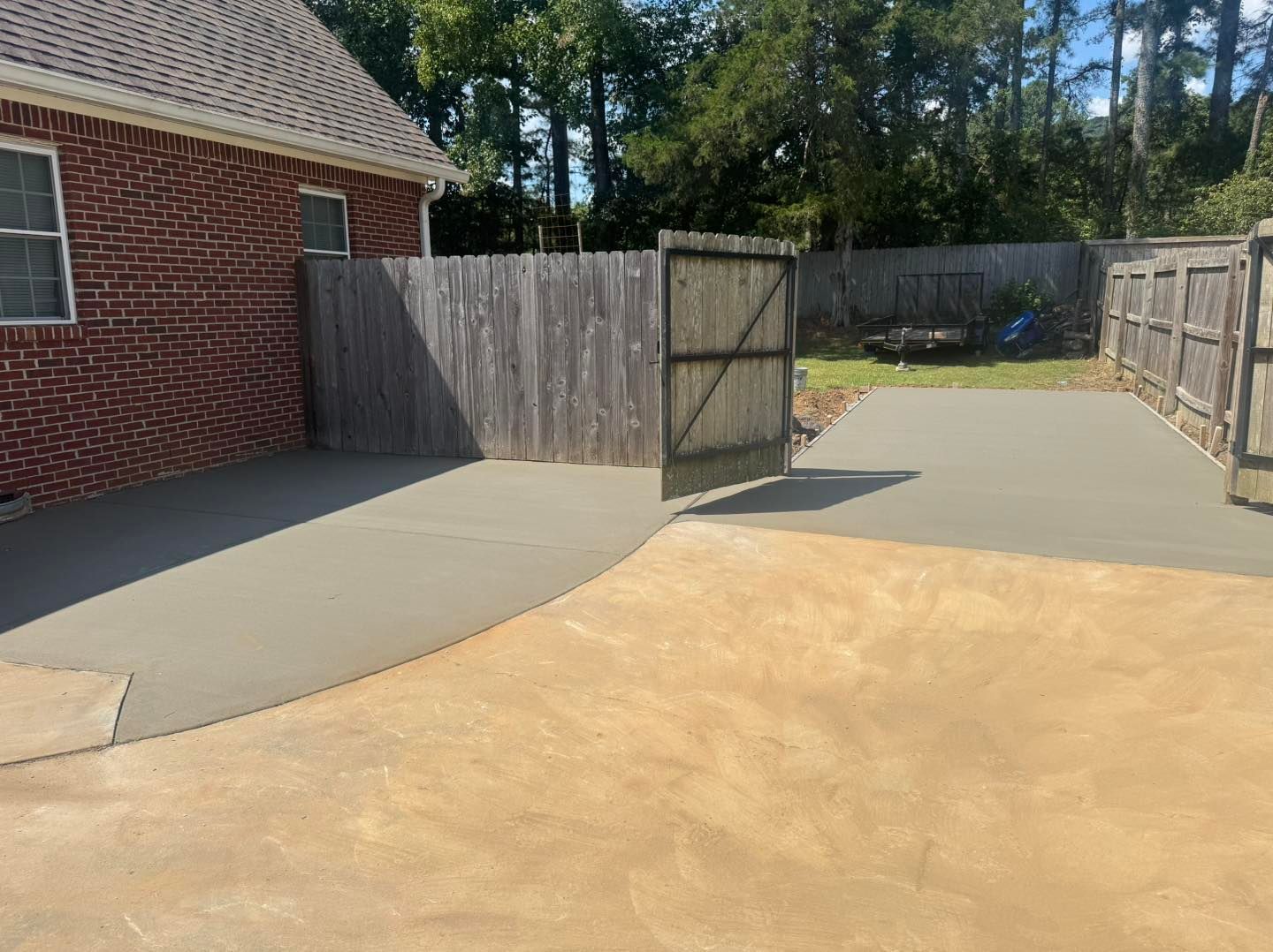 Backyard patio with open gate, concrete slab, wooden fence, and brick house exterior
