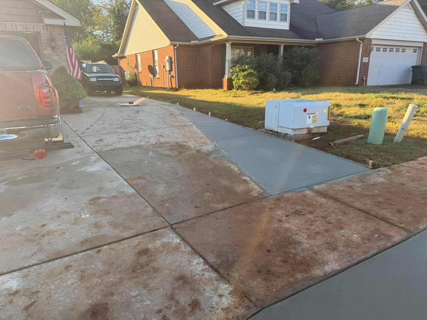 Driveway and sidewalk with wet pavement, a parked car, and a white utility box near brick houses.