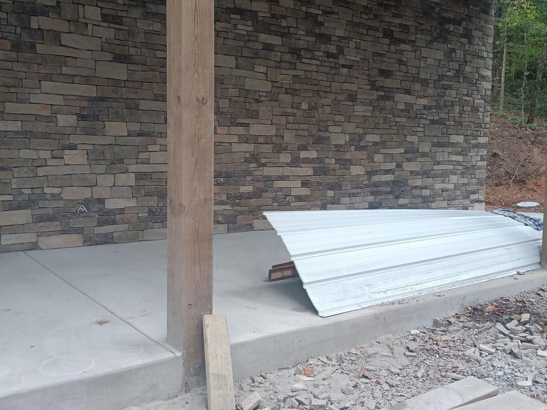 Corrugated metal sheet leaning on a concrete walkway beside a stone wall and wooden post