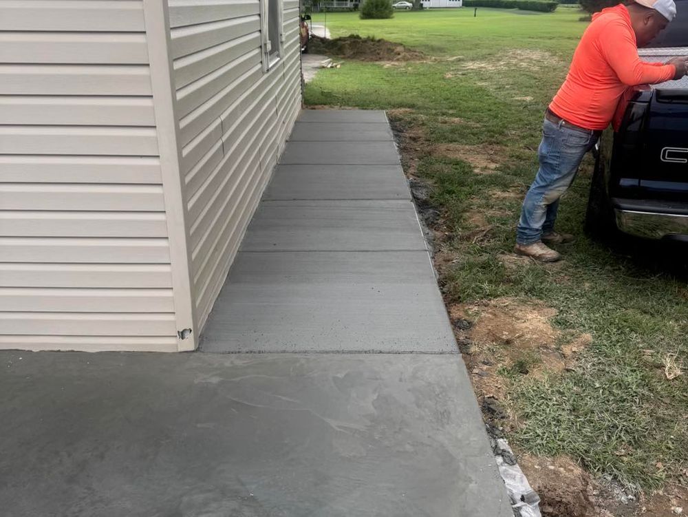 Person in orange jacket standing by a black vehicle beside a house and concrete walkway.