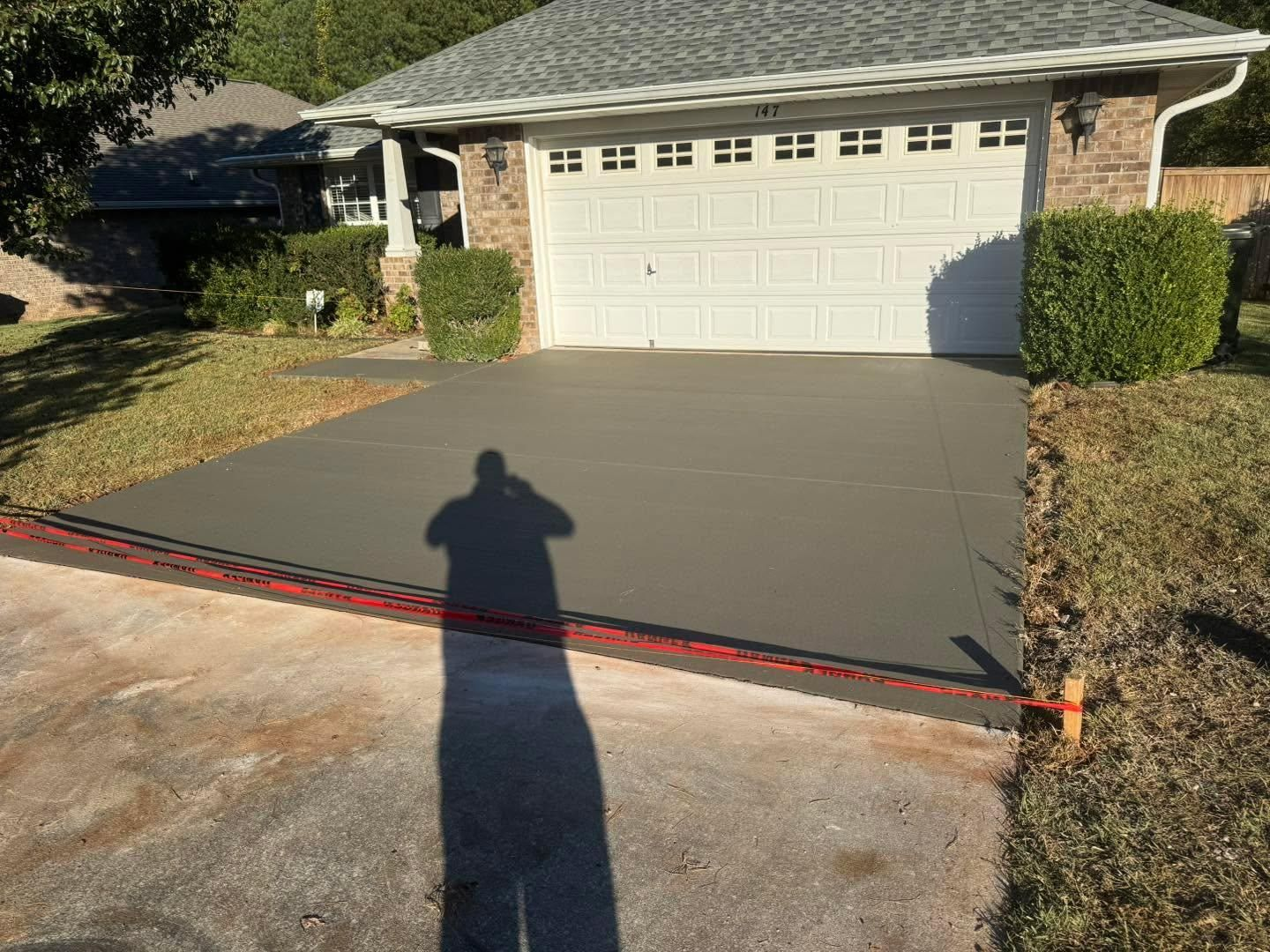 Freshly poured concrete driveway leading to a white garage, with a long shadow in the foreground.
