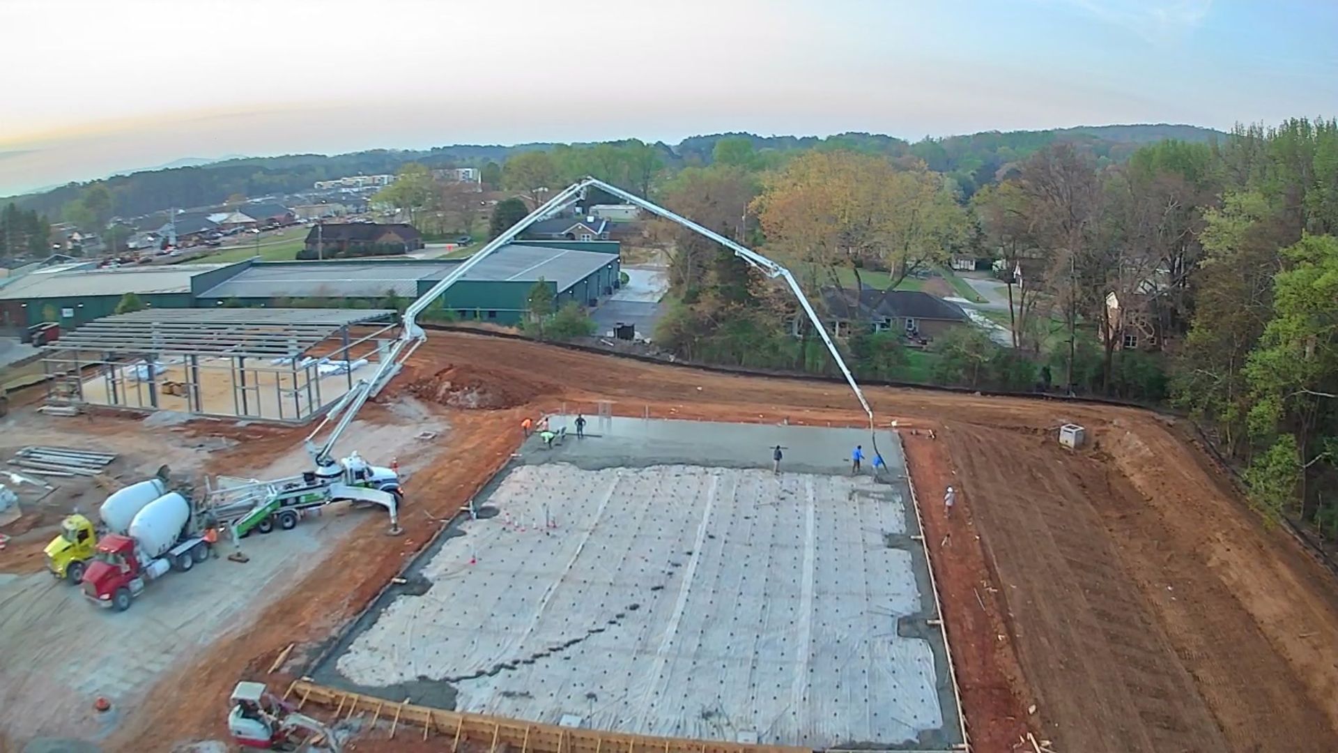 Construction site with concrete slab, workers, and a long white boom pouring concrete over a large foundation