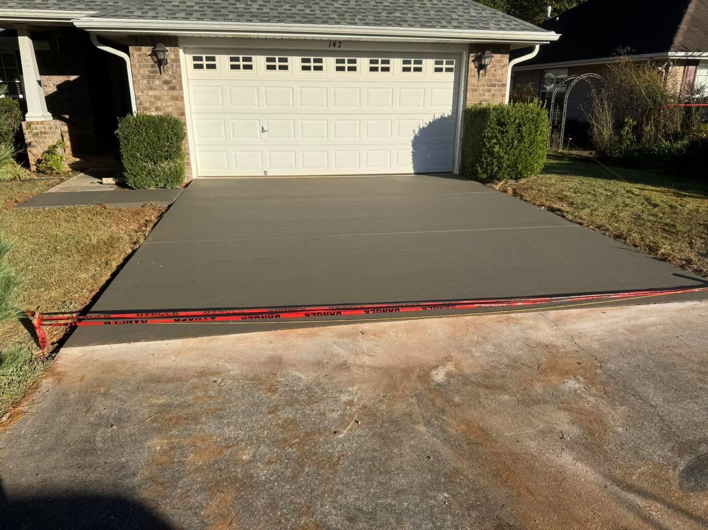 New concrete driveway in front of a white garage, with a red-marked edge near the street.