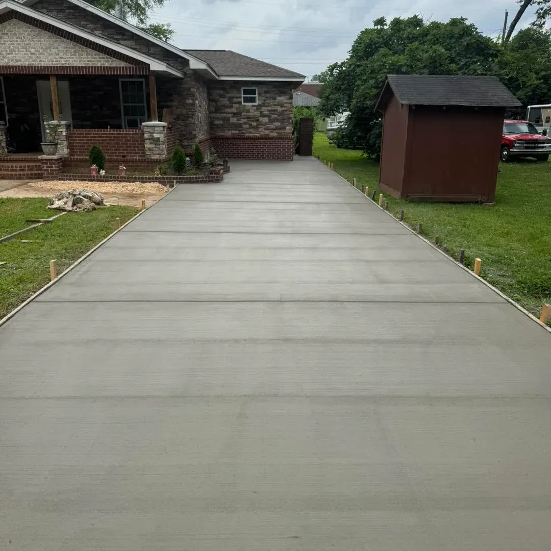 Concrete driveway leading to a brick house, with a small red shed and green lawn on the right.