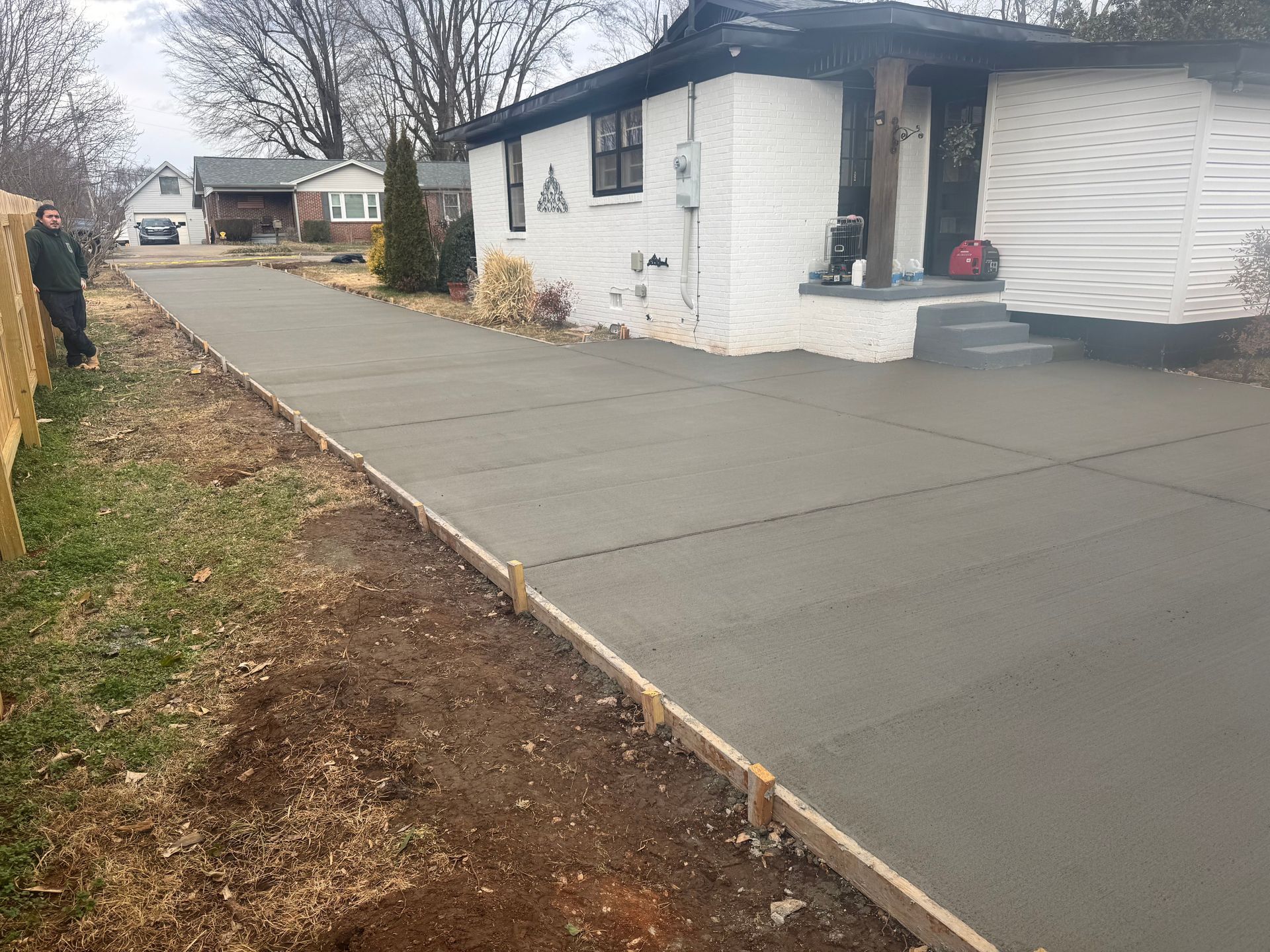 Freshly poured concrete driveway beside a white house with black trim, leading to the front steps.