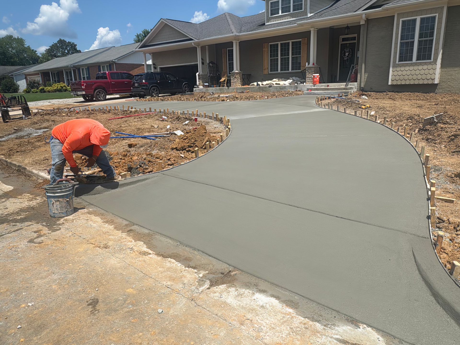Worker smoothing fresh concrete driveway at a new home construction site