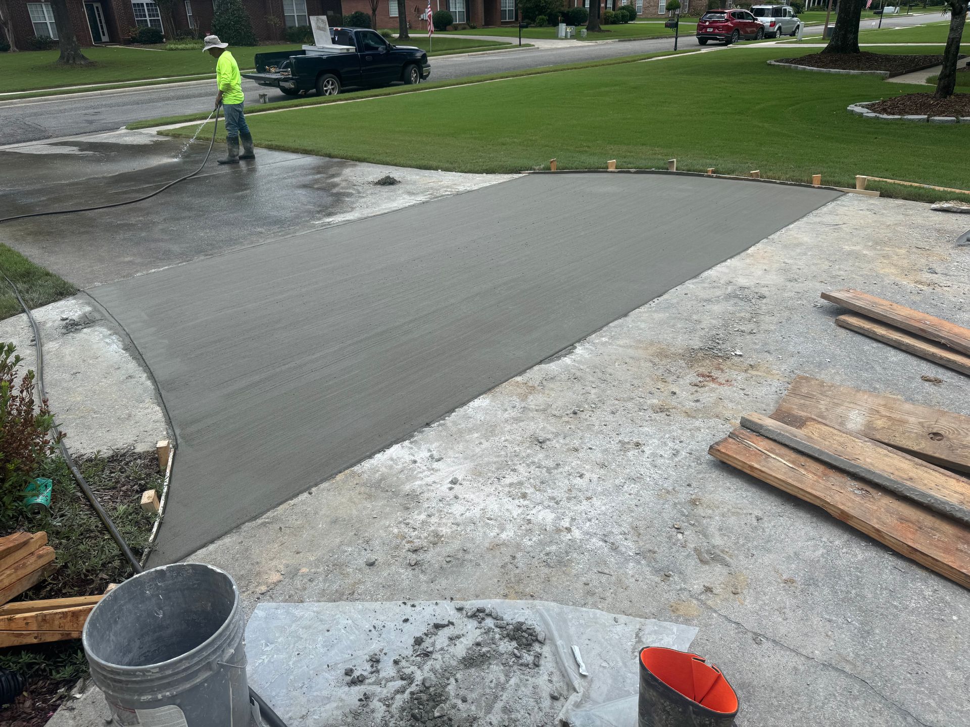 Fresh concrete driveway being smoothed, with a worker in a safety vest in the background.