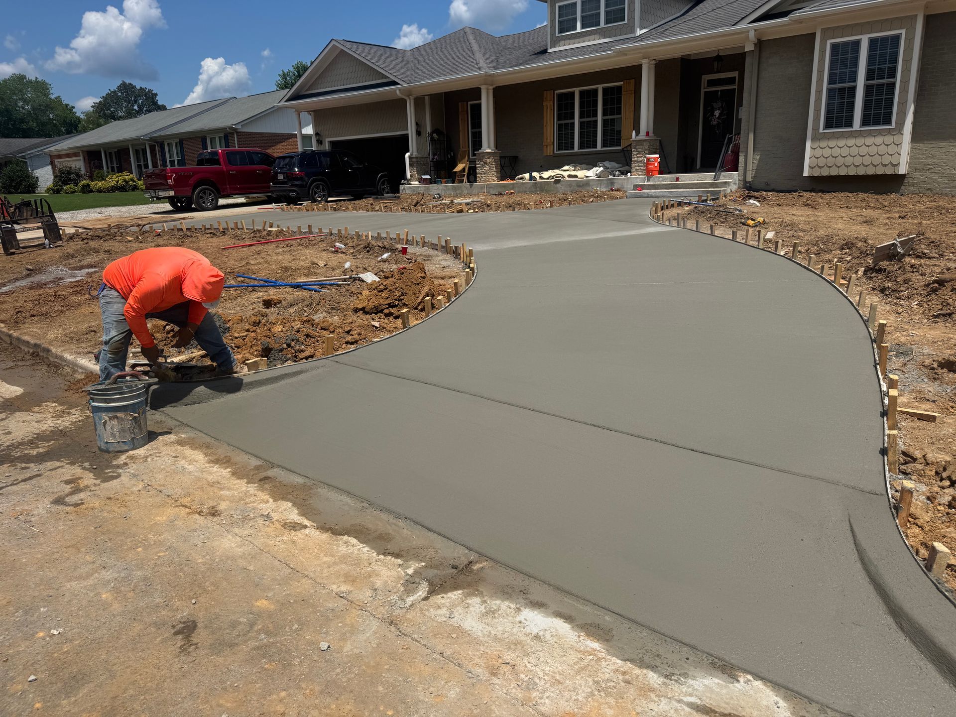 Worker smoothing fresh concrete driveway beside a house under construction
