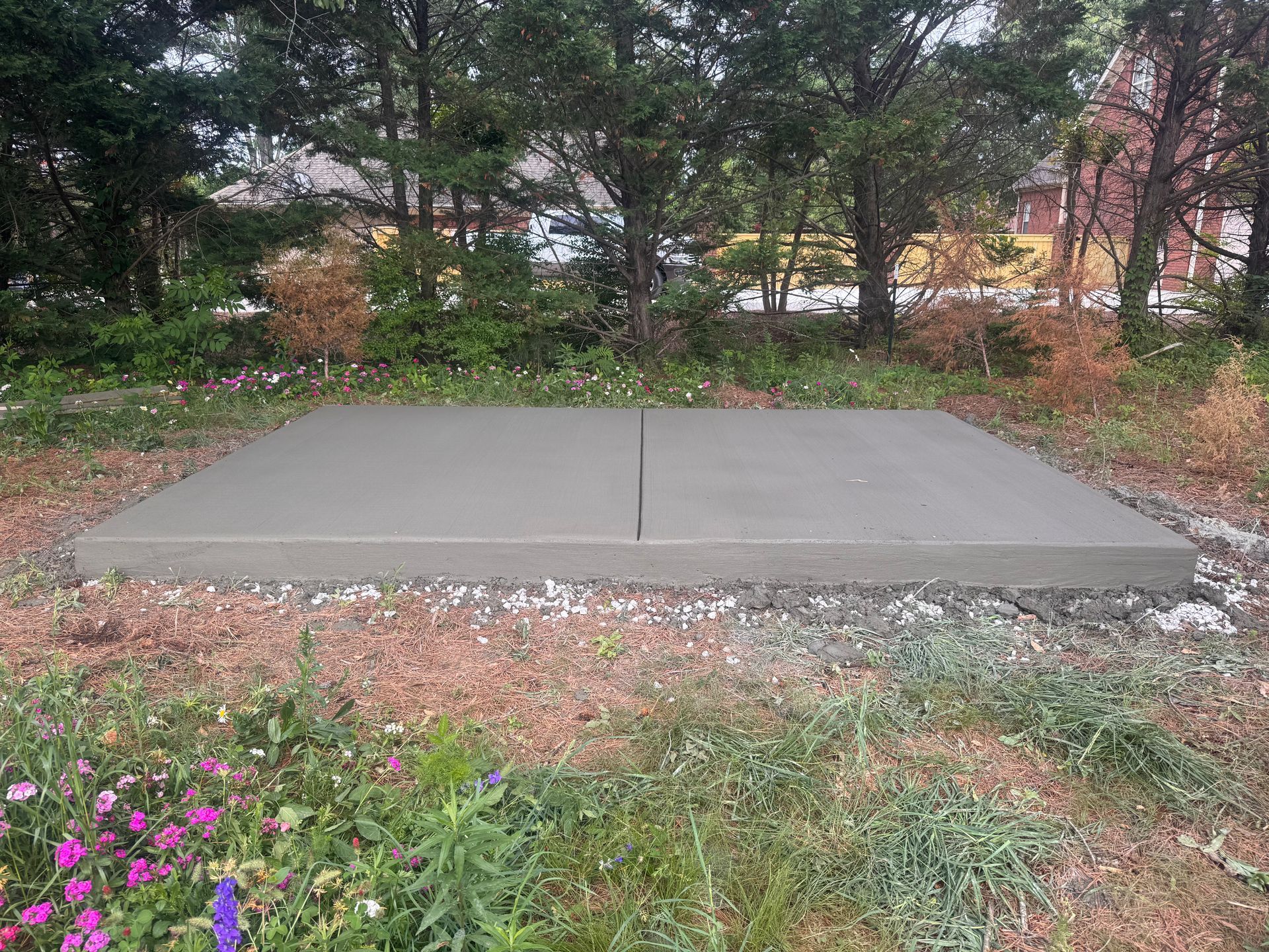 Concrete utility pad in a grassy yard with trees and flowers in the background