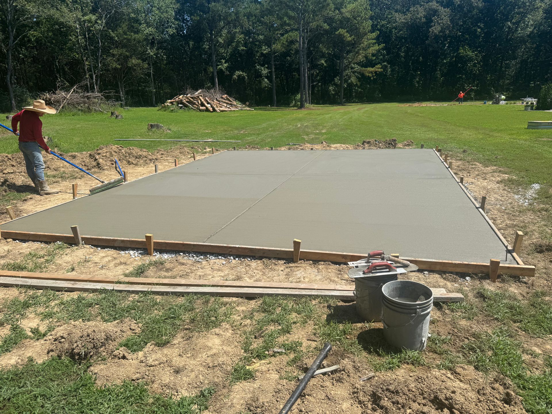 Freshly poured concrete slab being finished at a construction site, with a worker at the left edge.