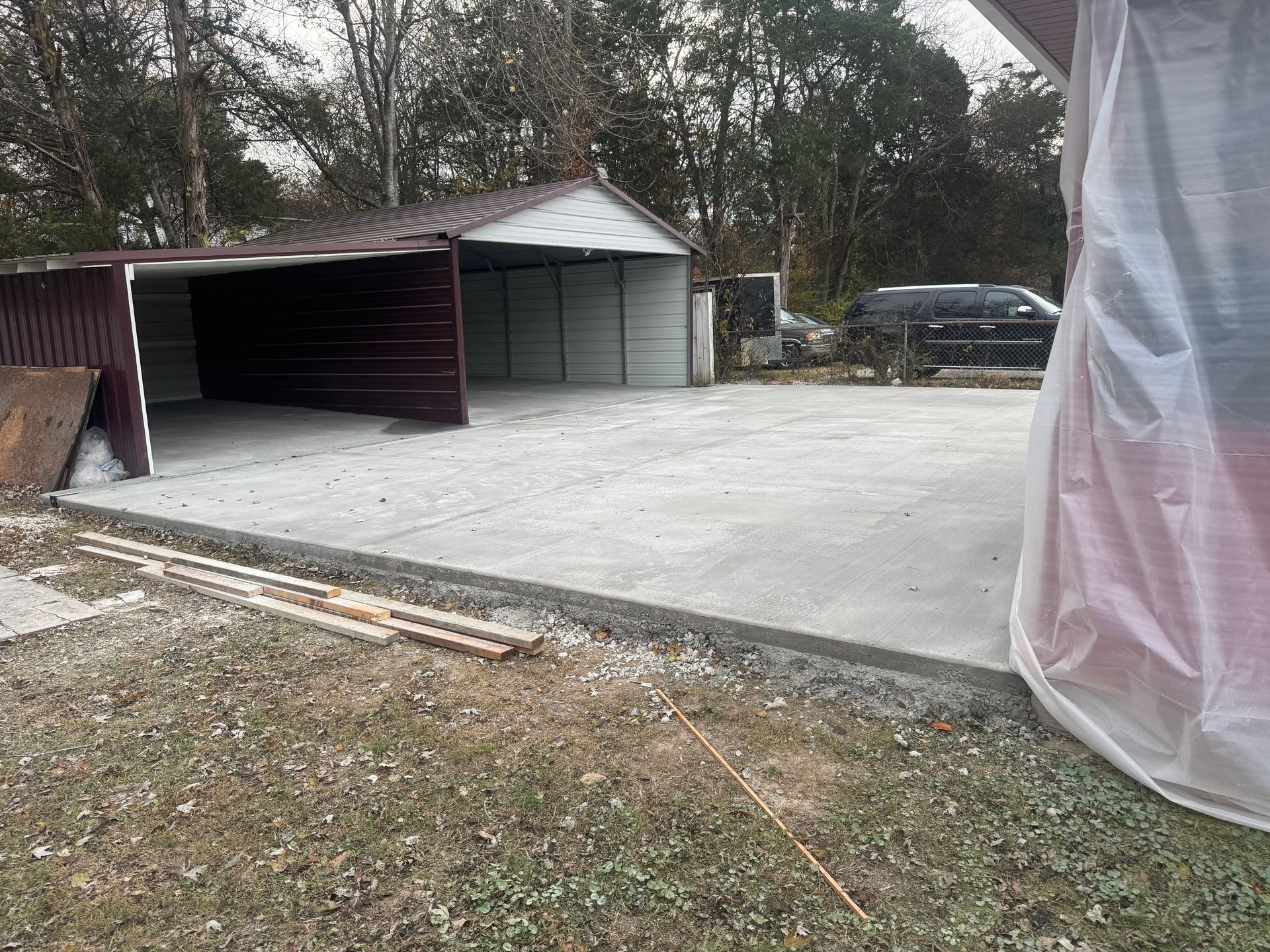 Concrete driveway with detached garage and open carport in a wooded yard