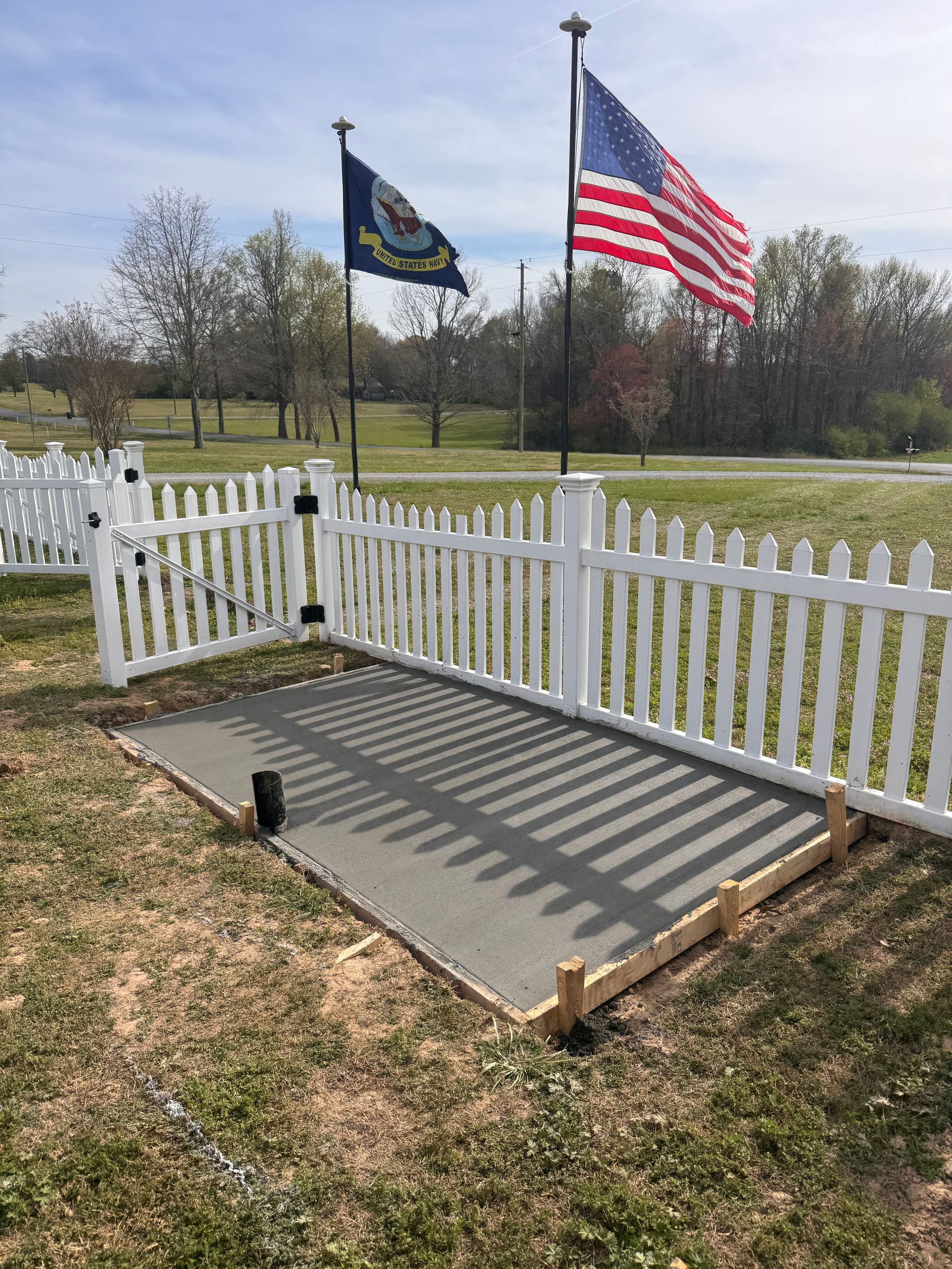 Small fenced memorial platform with two flags, including a U.S. flag, in a grassy field.