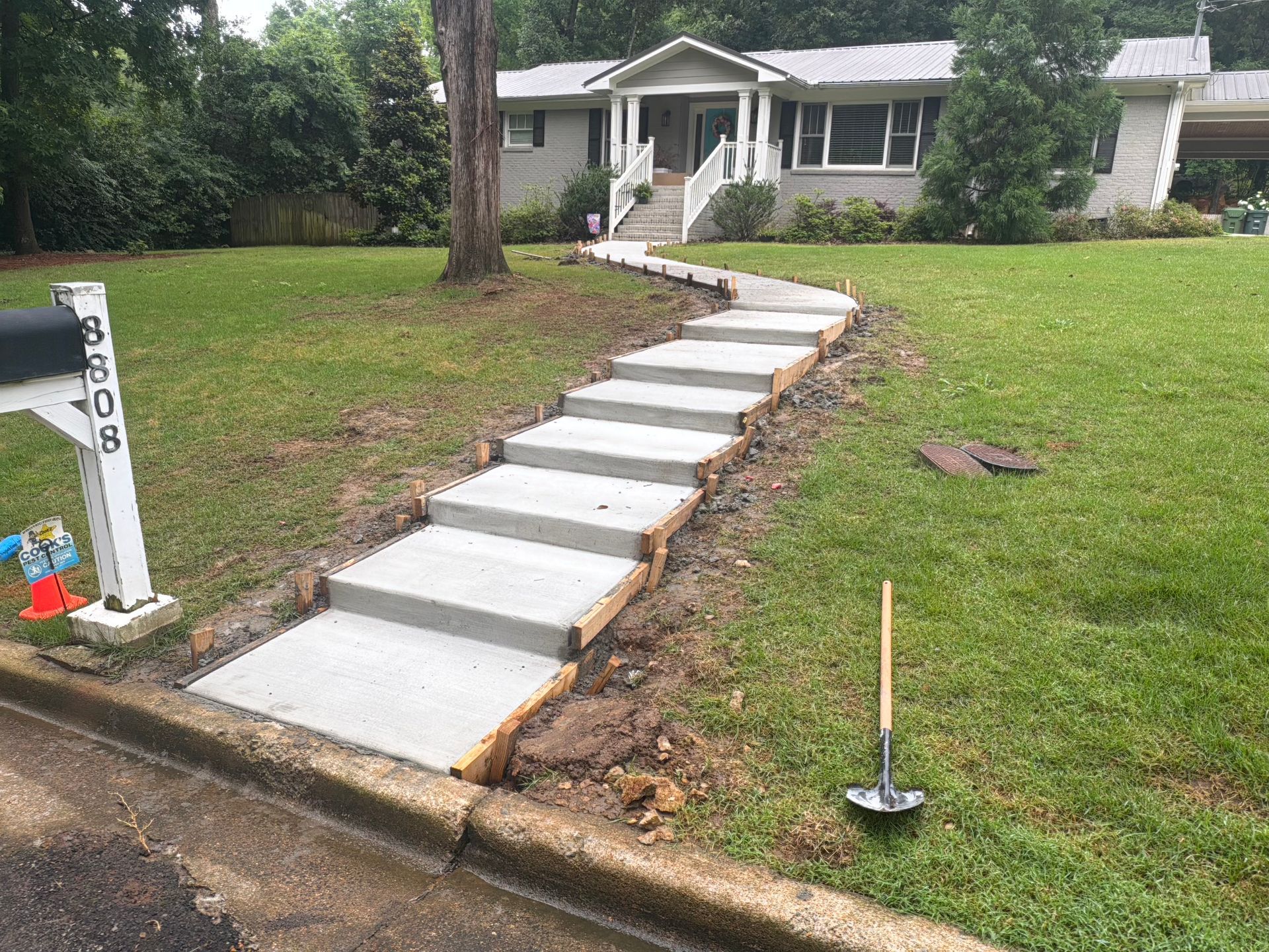 Concrete walkway under construction leading to a white house across a grassy front yard