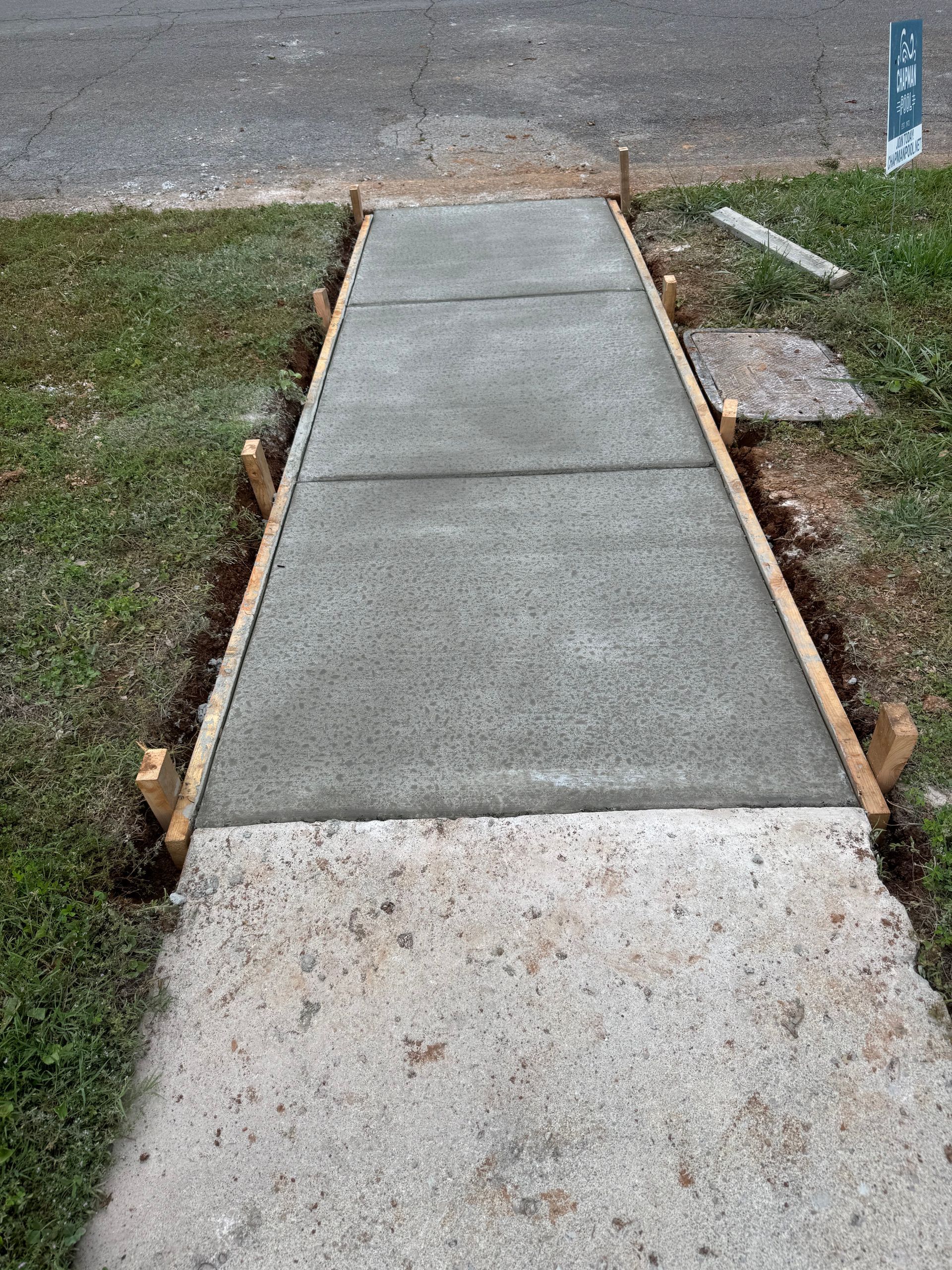 Concrete sidewalk ramp leading to the street, bordered by grass and a curb cut.