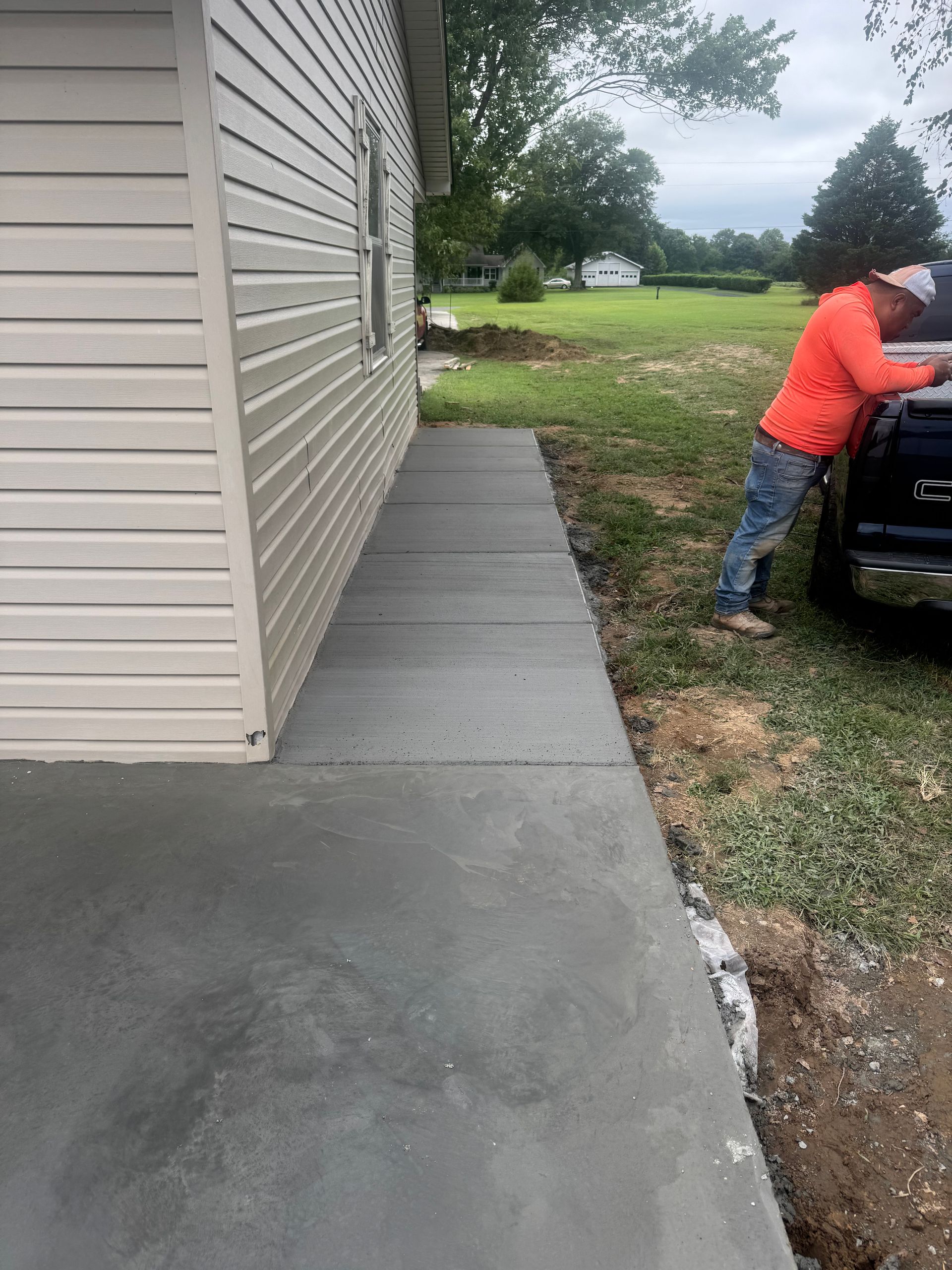 Concrete walkway beside house as a person in a red jacket leans into a black vehicle on the right.