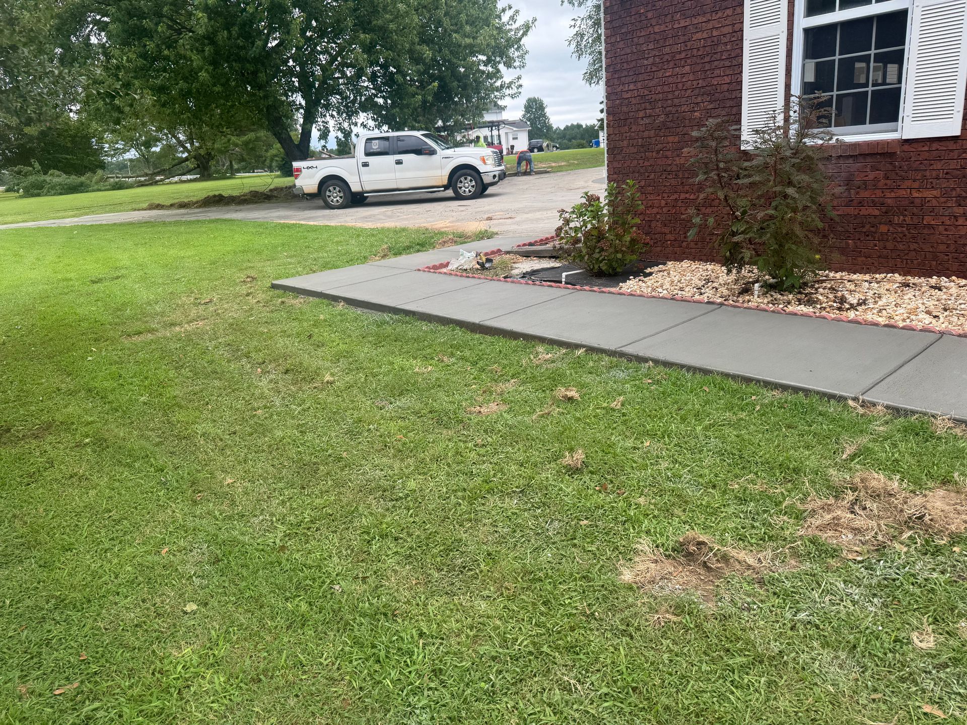Lawn beside a brick house with a sidewalk; a white pickup truck is parked near the driveway.