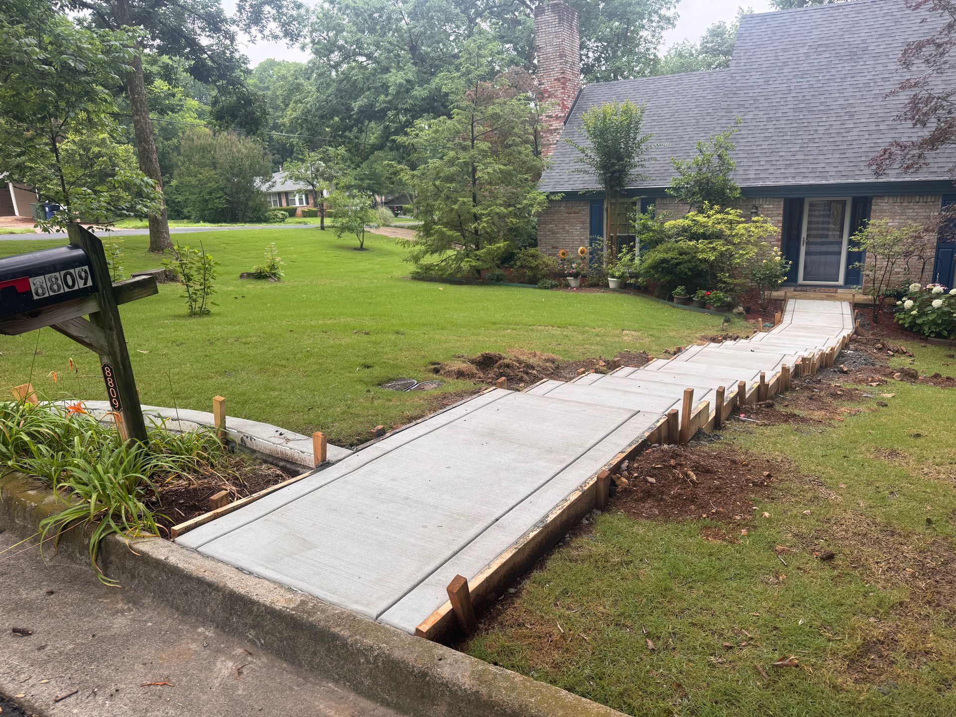 Concrete walkway leading to a house entrance, bordered by fresh soil and greenery after construction