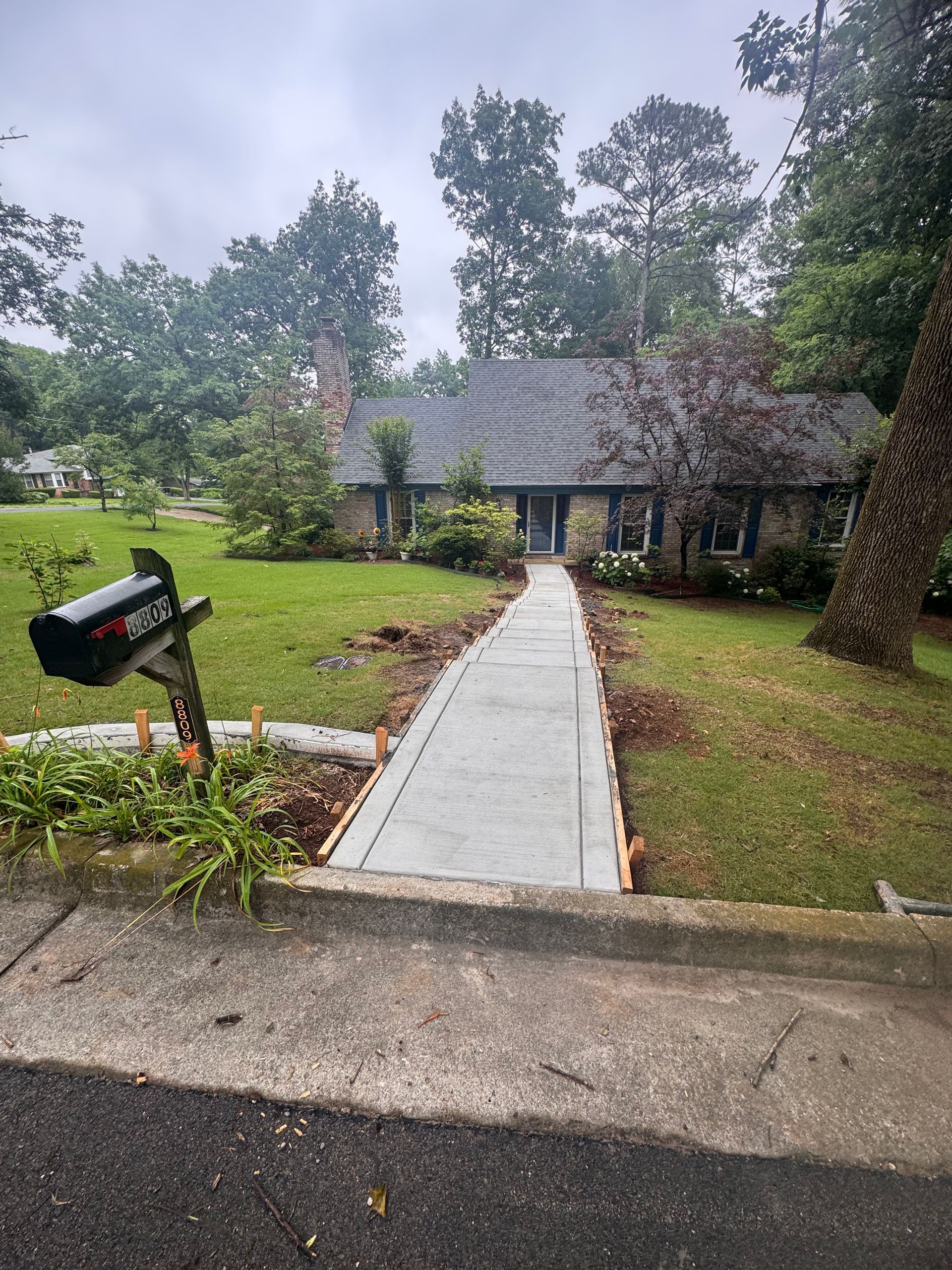Front walkway leading to a brick house with a black mailbox and green lawn