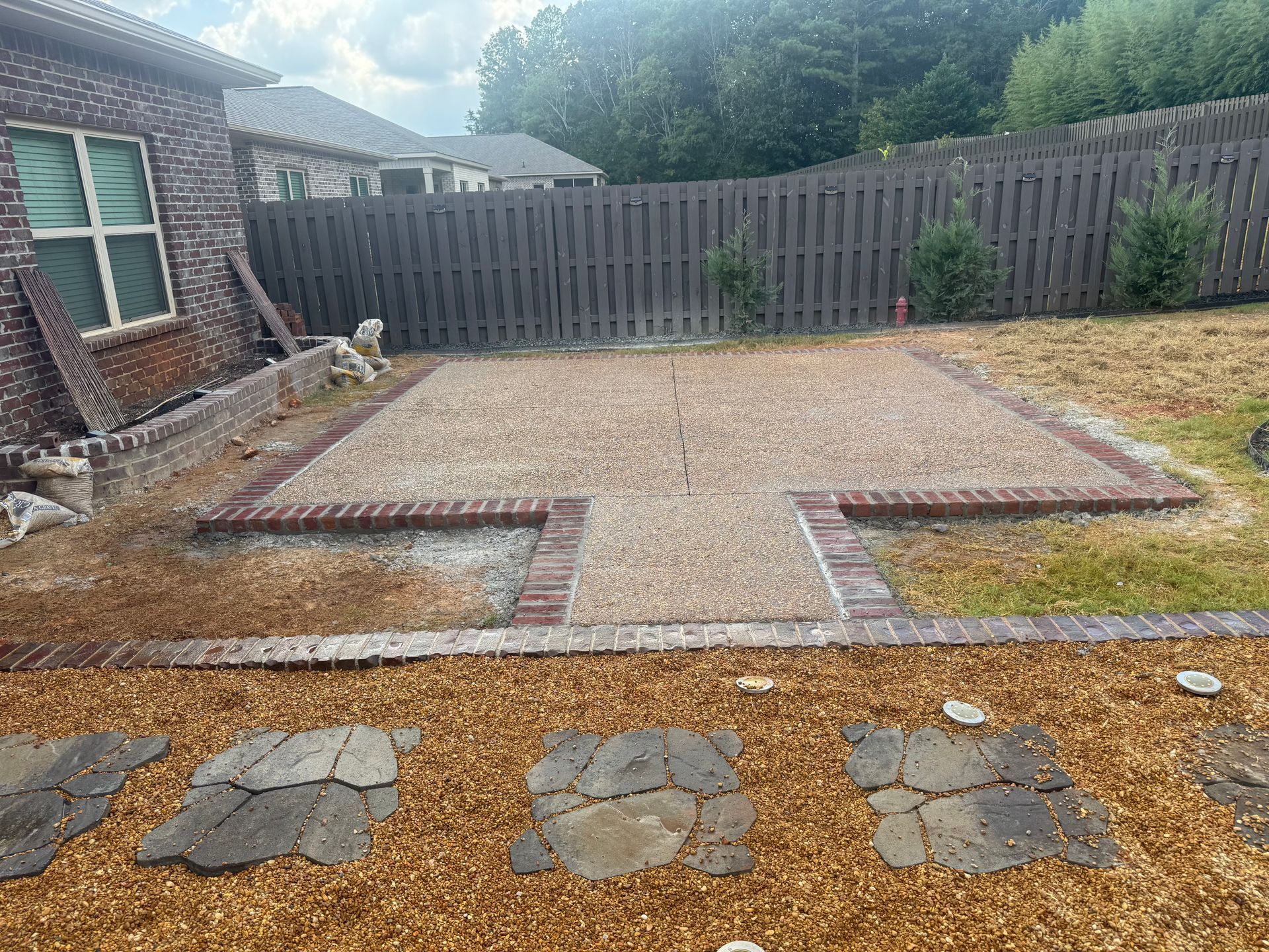 Backyard patio under construction with gravel, paver foundation, and wooden fence backdrop