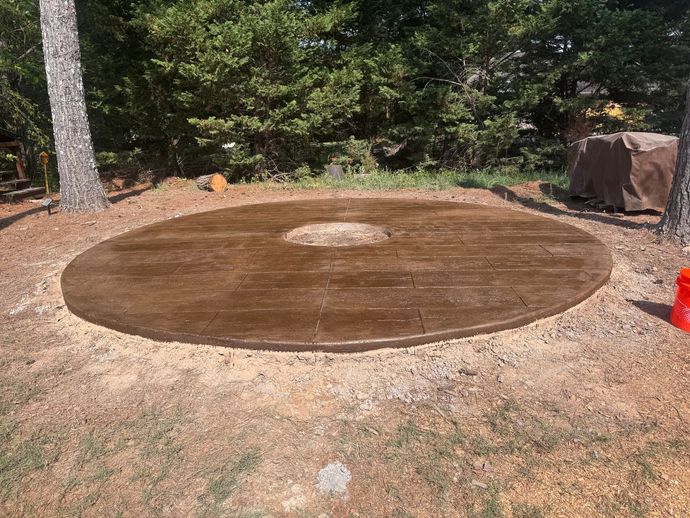 Large circular brown tarpaulin laid on dirt in a wooded outdoor area, with a few rocks and a cone nearby