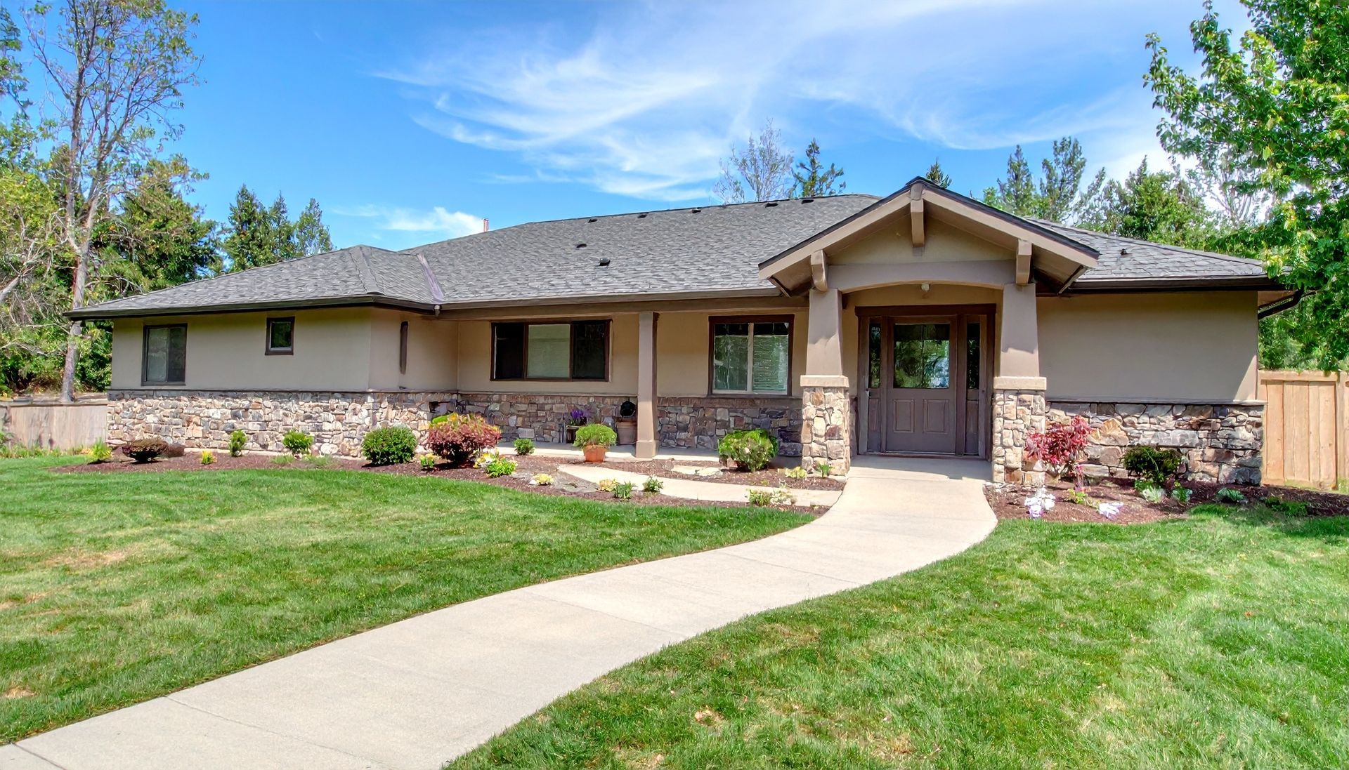 Single-story tan house with stone accents, front lawn, and curved concrete walkway under a blue sky