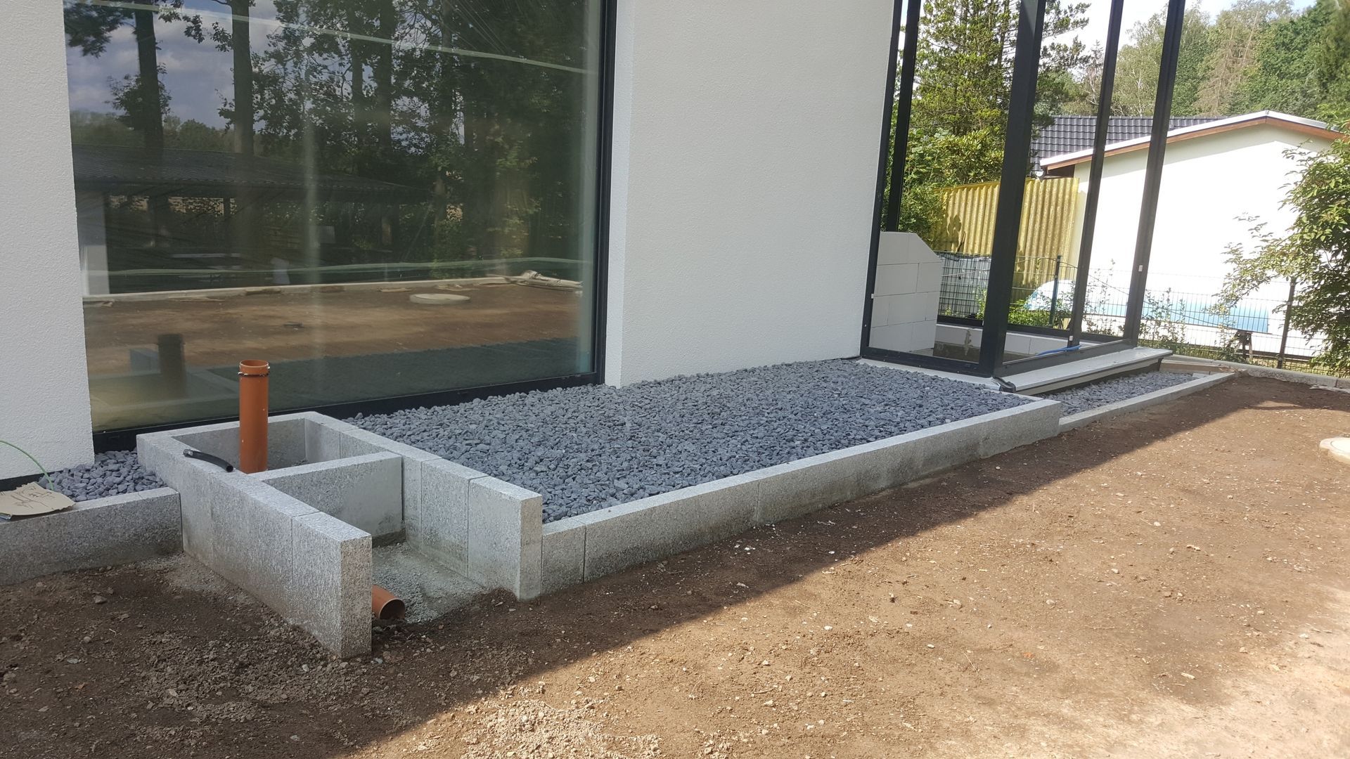 Modern house exterior with gravel drainage bed, concrete planter, and dirt yard beside large windows