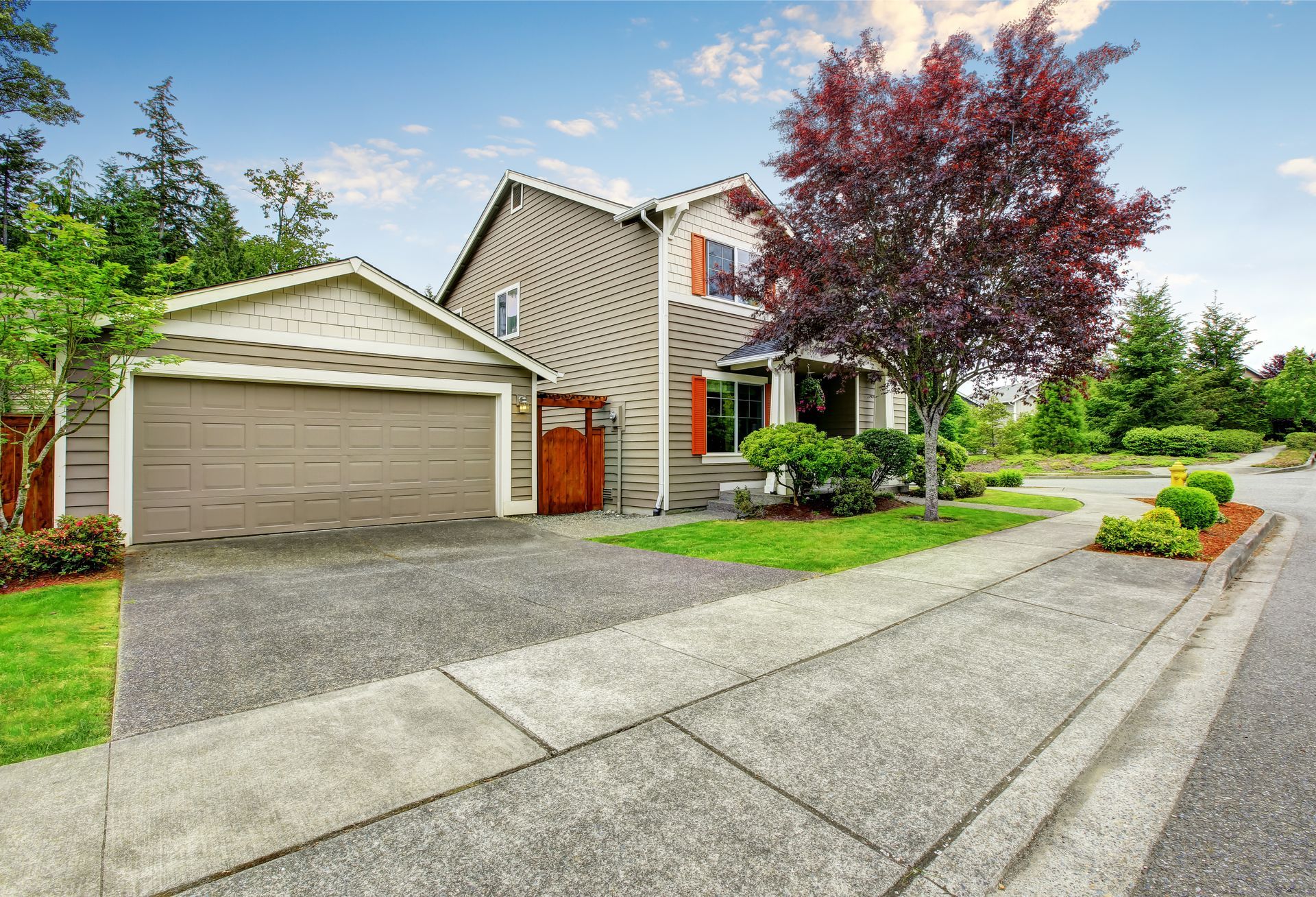 Suburban house with beige siding, two-car garage, driveway, and a red-leaf tree along a quiet street