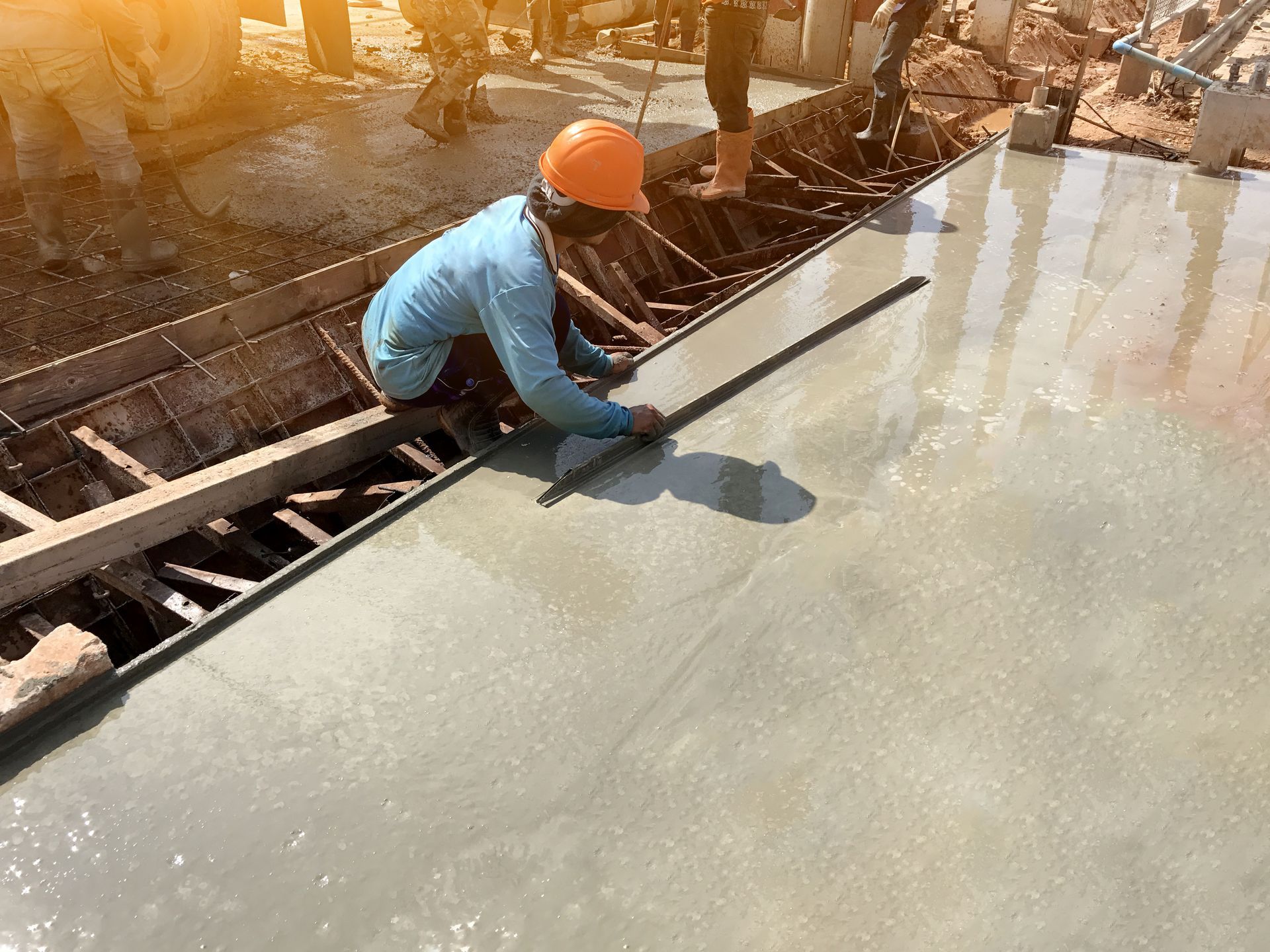 Worker in an orange hard hat smoothing wet concrete at a construction site.