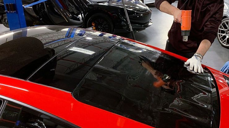 A man is applying tint to the windshield of a red car.