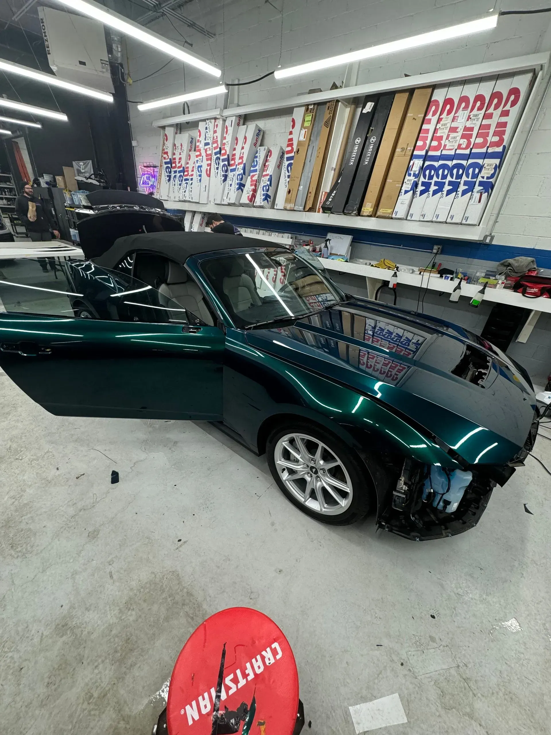 Green sports car in an auto shop, with its door open and its hood raised.