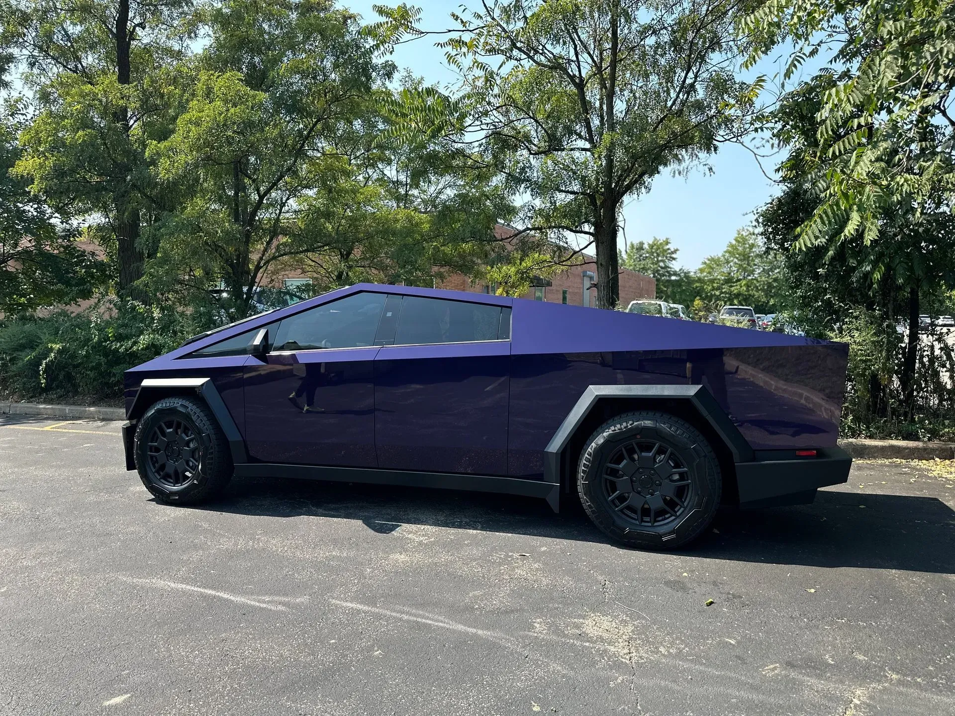 Purple futuristic pickup truck parked on a sunny street with trees in the background