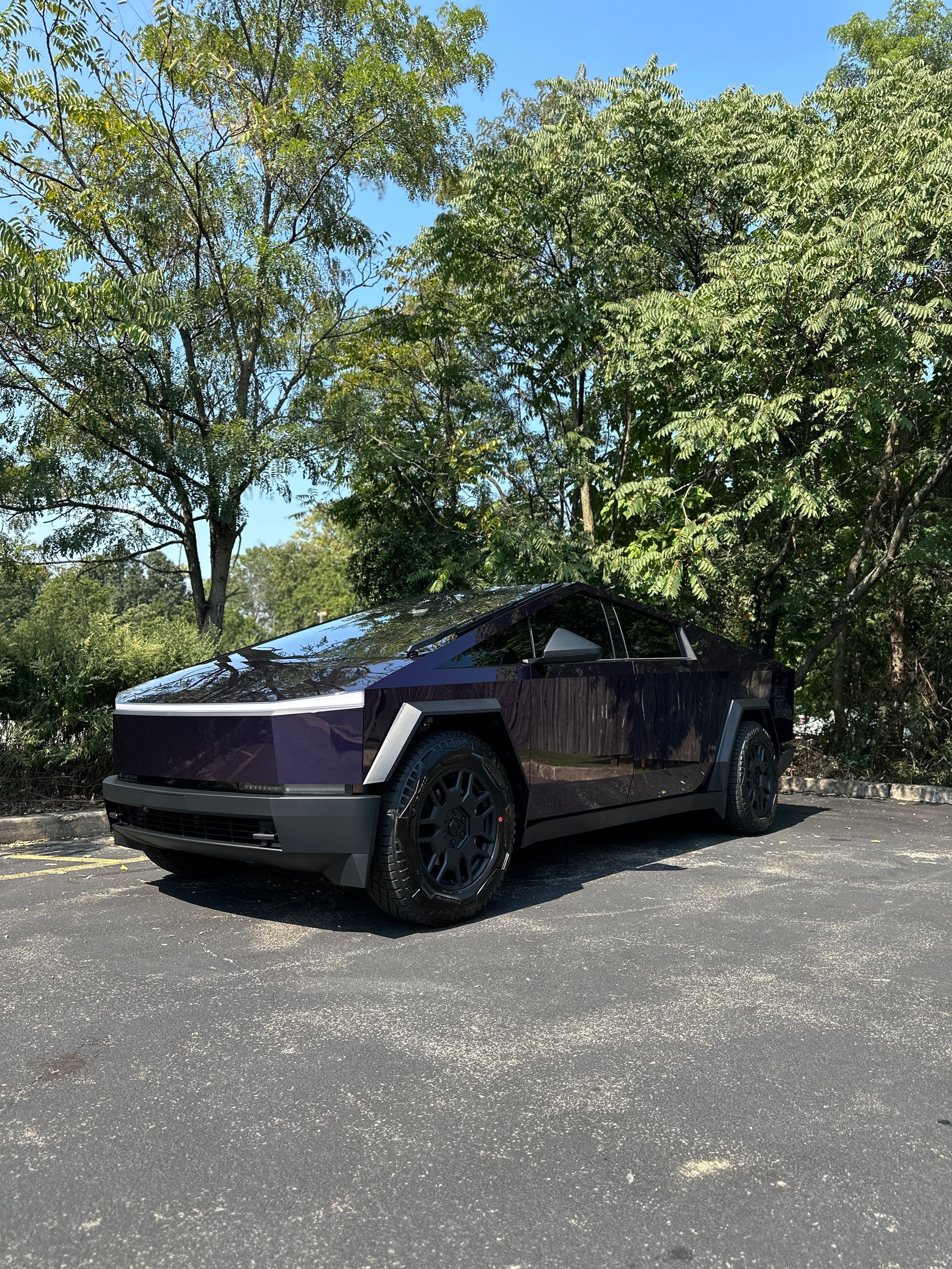 A purple tesla model s is parked in a parking lot surrounded by trees.