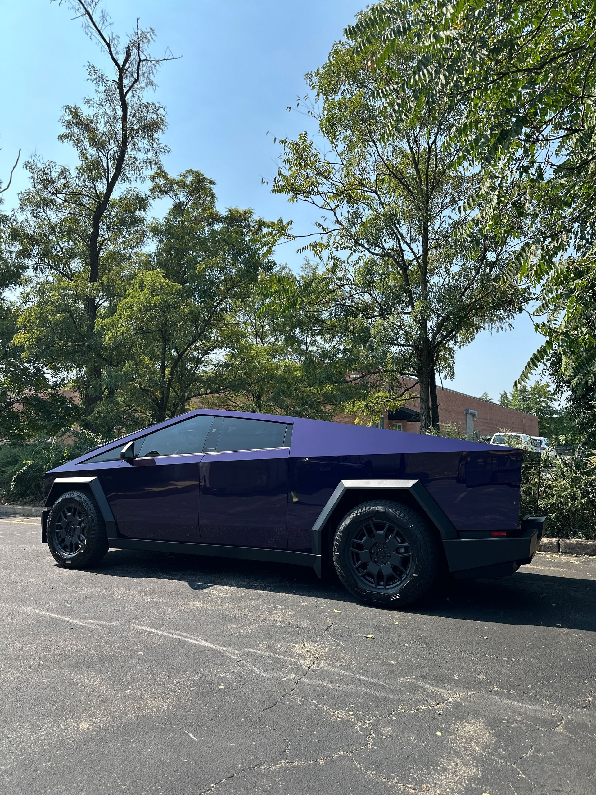 A purple car is parked in a parking lot with trees in the background.