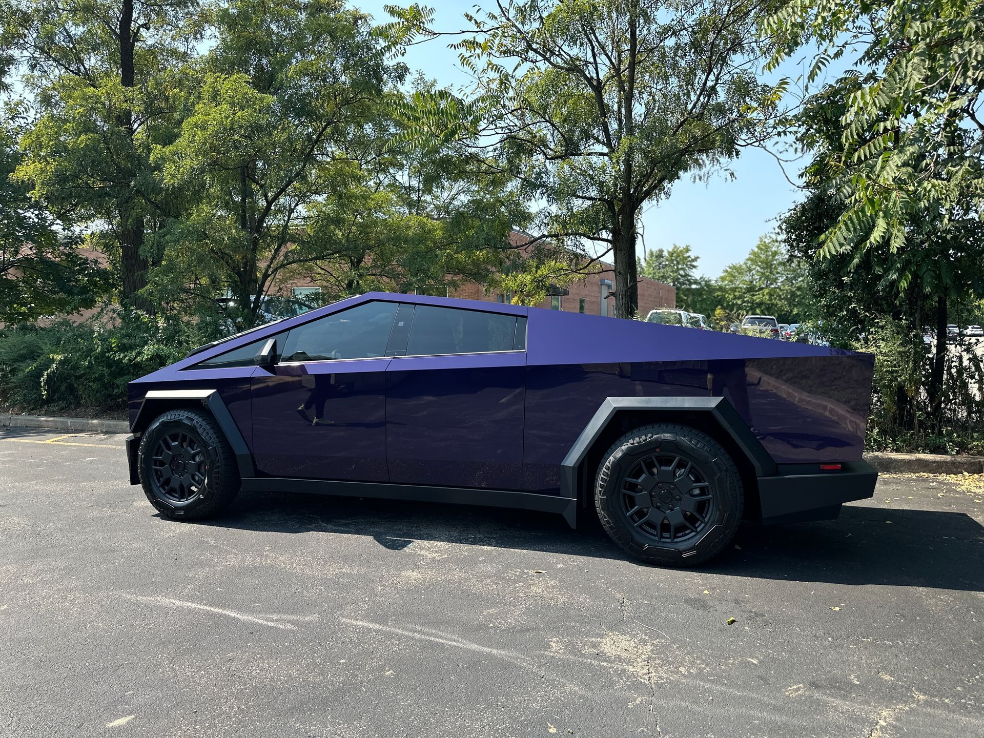A purple tesla cybertruck is parked in a parking lot.