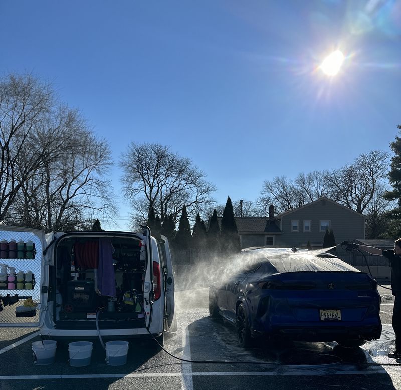 Open van with gear beside a blue car steaming in a snowy parking lot under bright sun