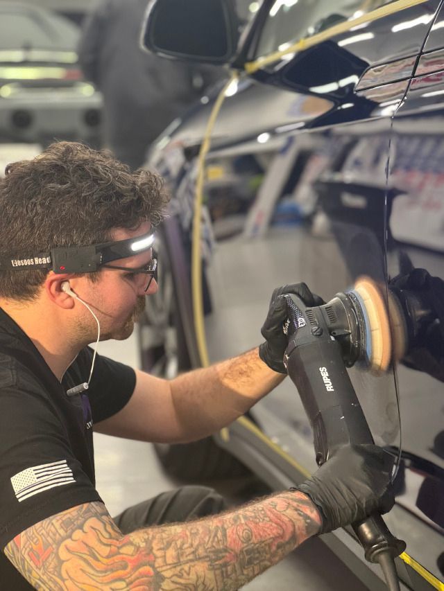 Person polishing a dark car with a power buffer in a garage