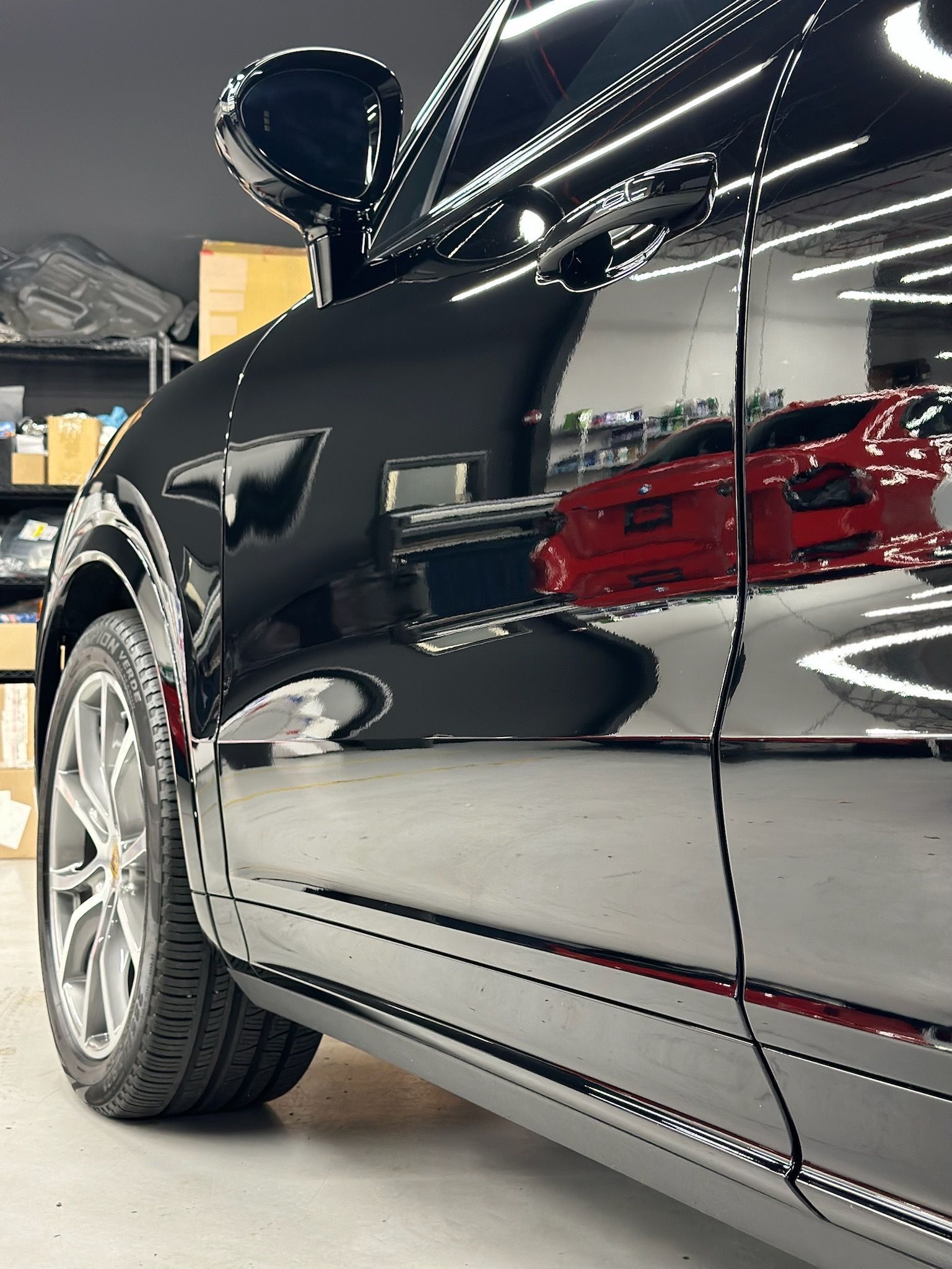 Close-up of a black car’s side panel and wheel in a showroom, with red reflections on the glossy paint