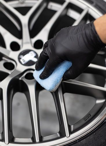A person wearing black gloves is cleaning a car wheel with a sponge.