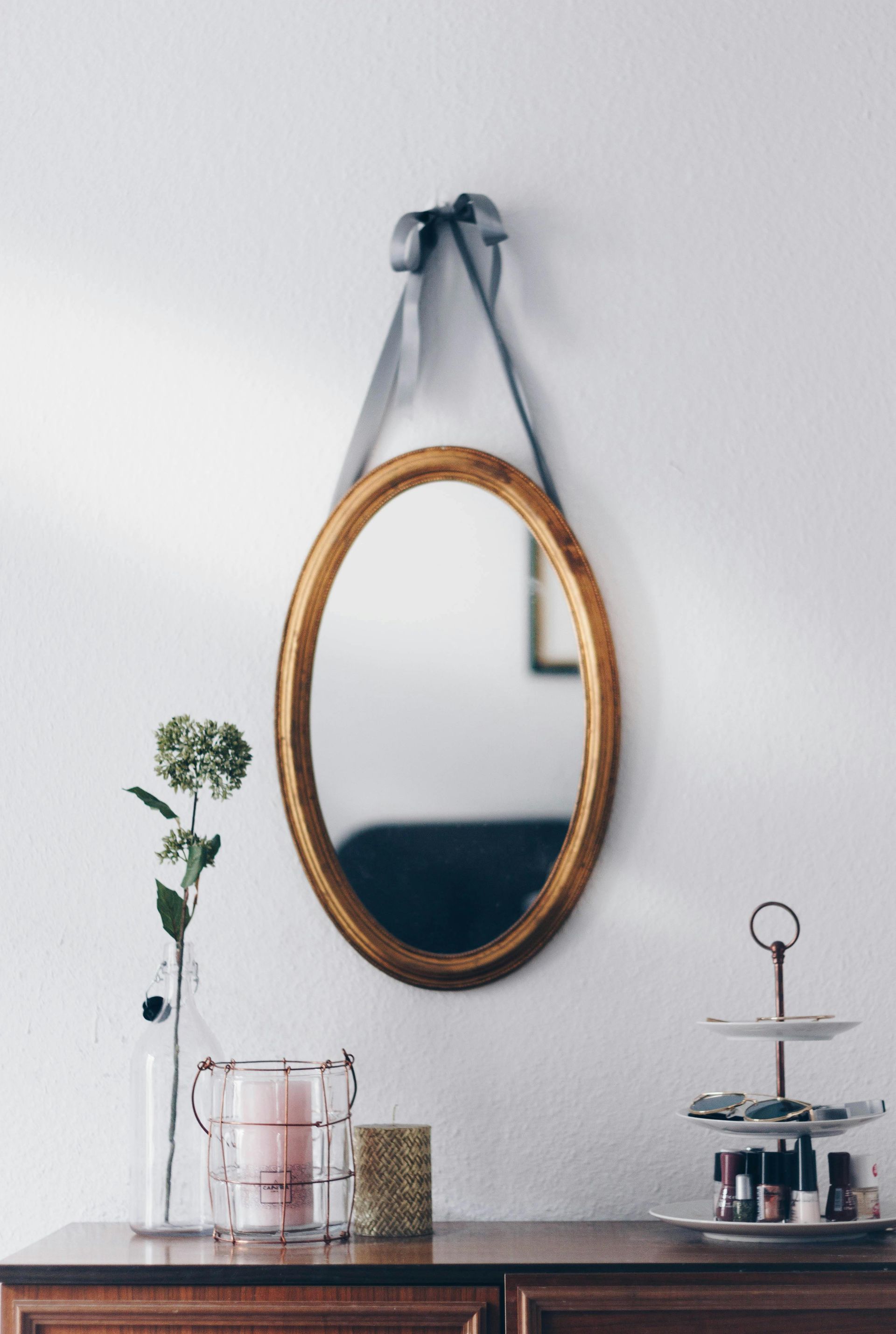 An oval mirror is hanging on a white wall