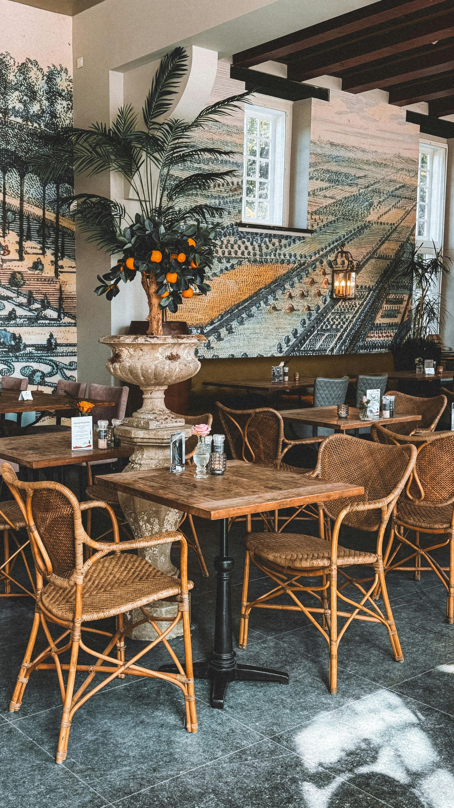 A restaurant with wicker chairs and tables and a vase of oranges on the wall.
